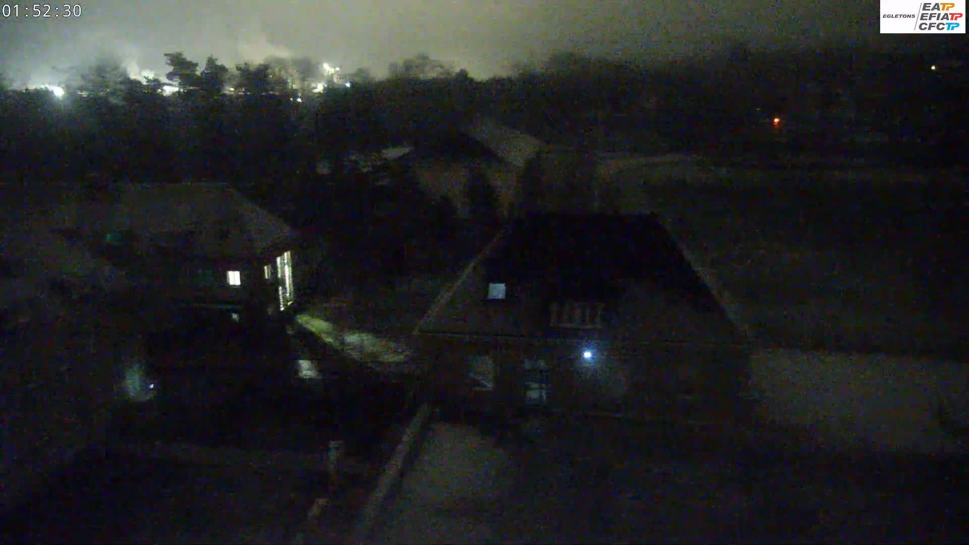 A nighttime aerial view shows a few buildings and trees under a dark, cloudy sky.