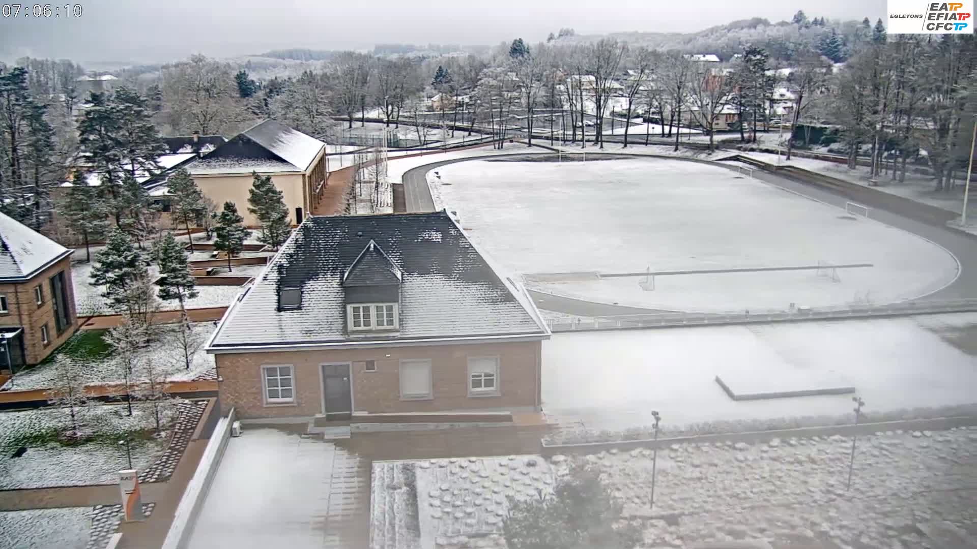 A snow-covered athletic field and several buildings are visible on a cloudy day.