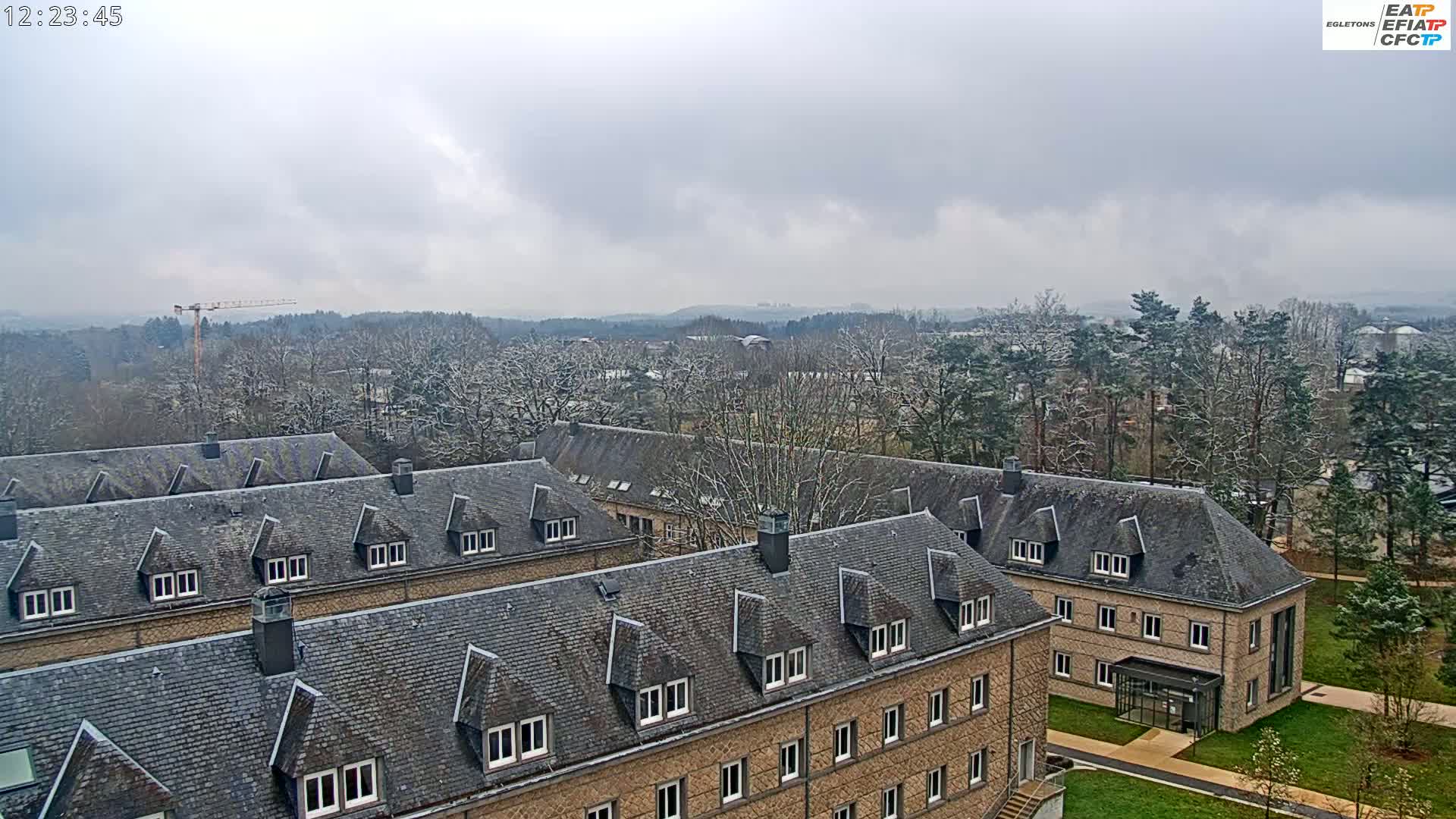 A snow-dusted landscape featuring a complex of buildings with gray slate roofs under an overcast sky.