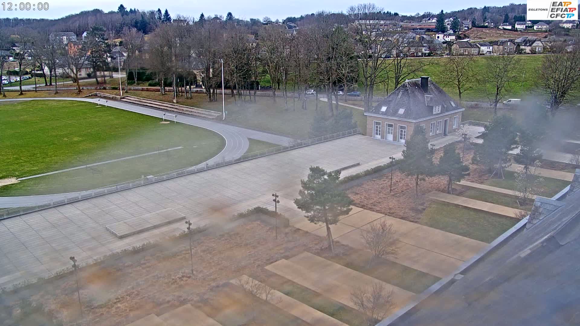 An aerial view shows a running track and a large building situated in a landscaped area on an overcast day.
