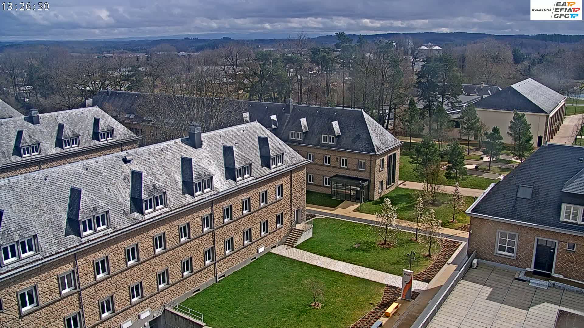 An aerial view of a campus with several stone buildings and grassy areas under a partly cloudy sky.