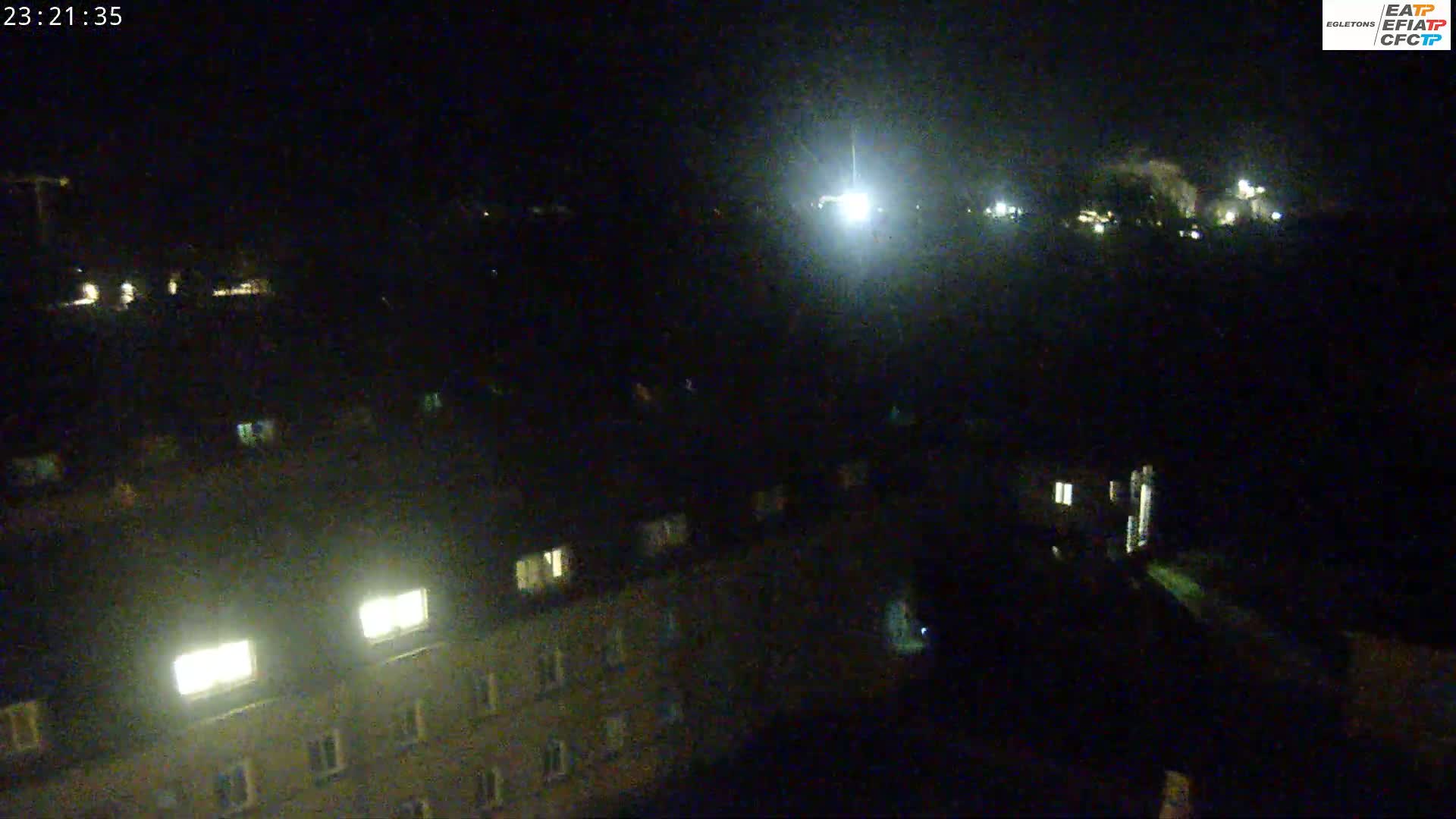 A nighttime, high-angle view of a residential area with dimly lit buildings and a few bright lights.