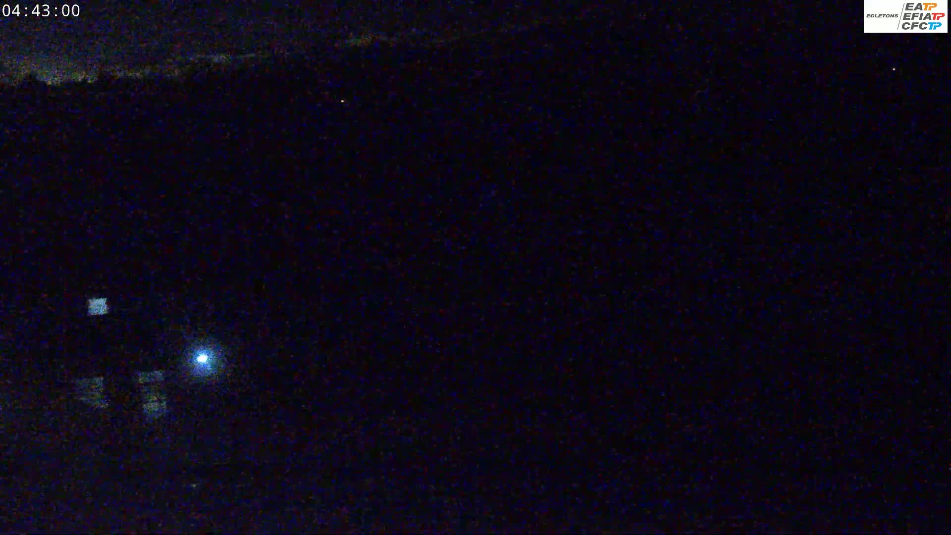 A nighttime, low-light view shows a dark landscape with a few faint lights visible in the distance.