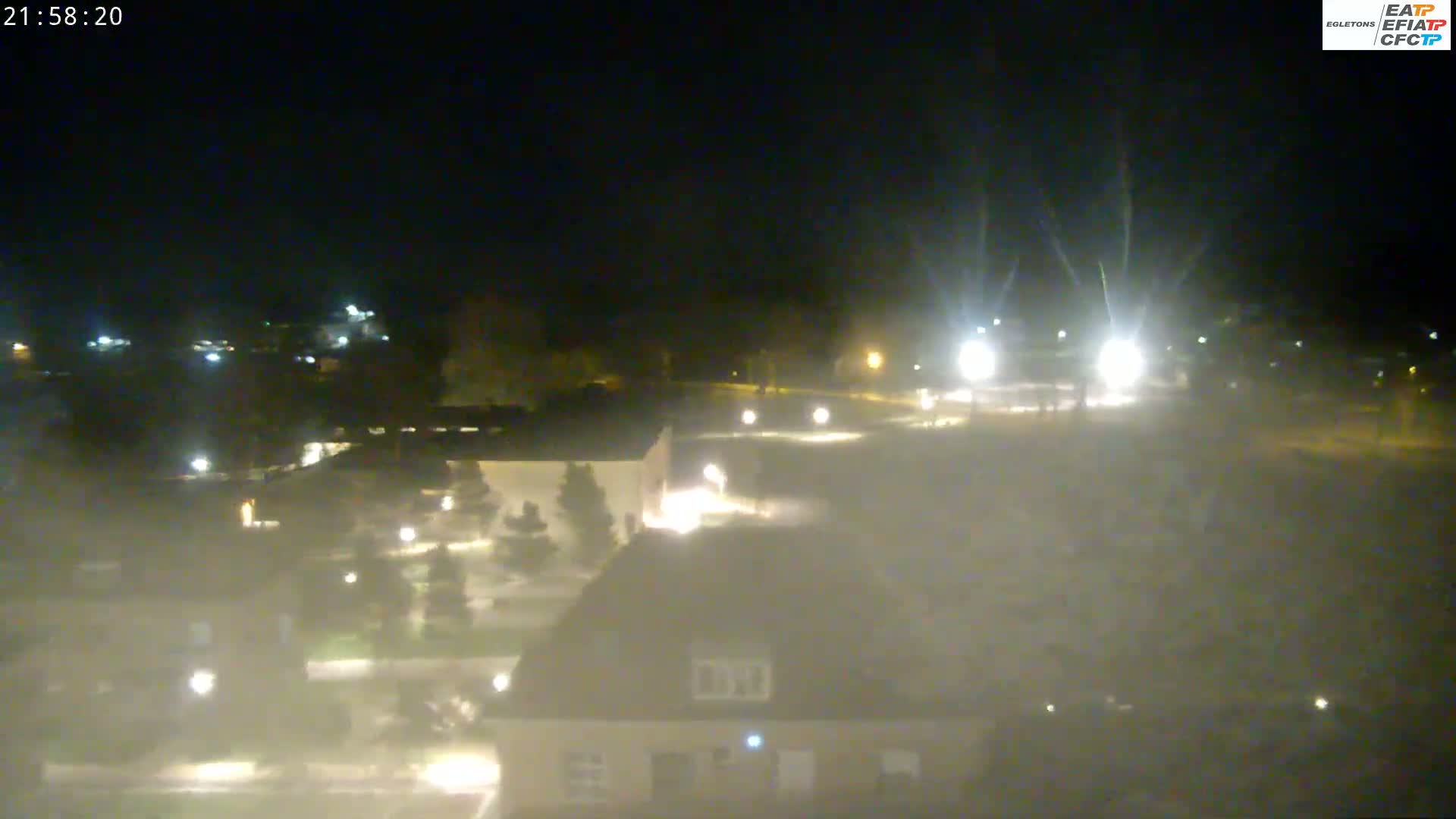 A nighttime, hazy view of a parking lot and buildings with scattered lights.