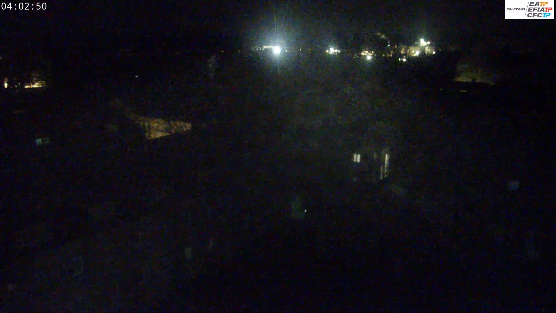 A nighttime, dark view of buildings and land with some faint lights visible in the distance.