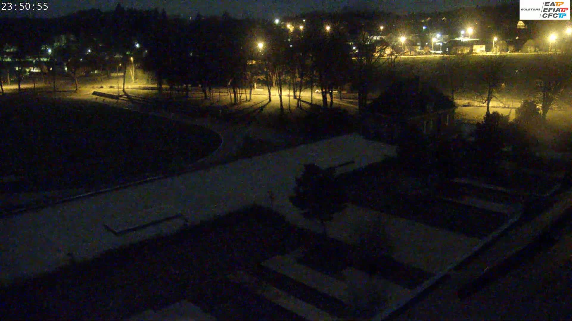 A nighttime aerial view shows a park with dimly lit pathways, trees, and buildings under a dark sky.