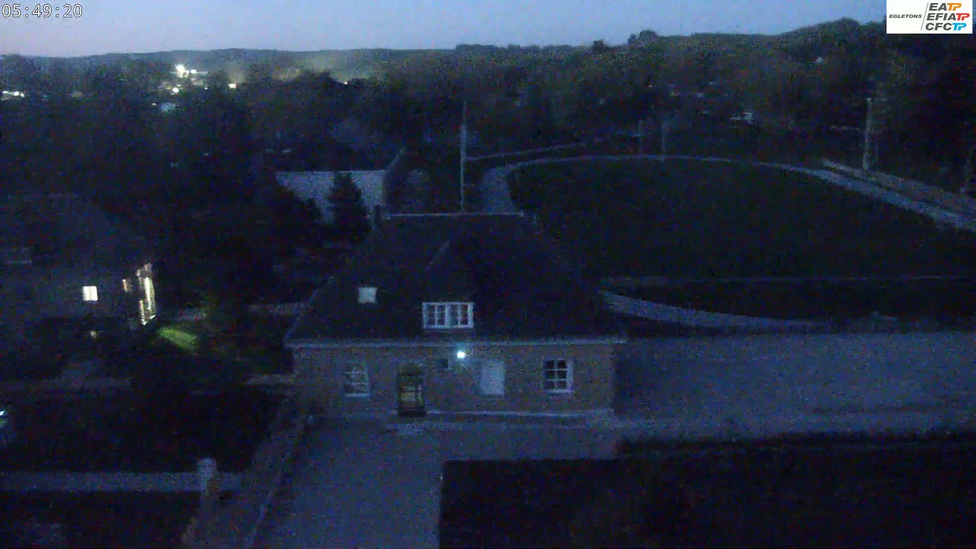 An aerial nighttime view shows a single-story building next to a dark green field under a twilight sky.