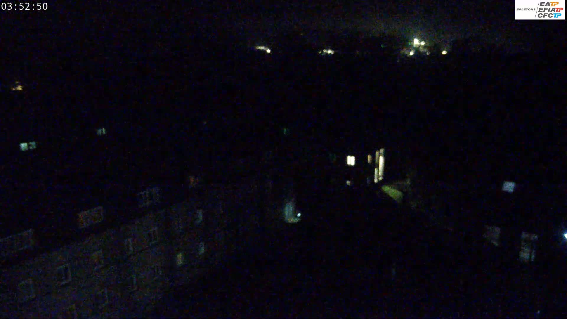 A nighttime, high-angle view shows a dark cityscape with sparsely lit windows in buildings.