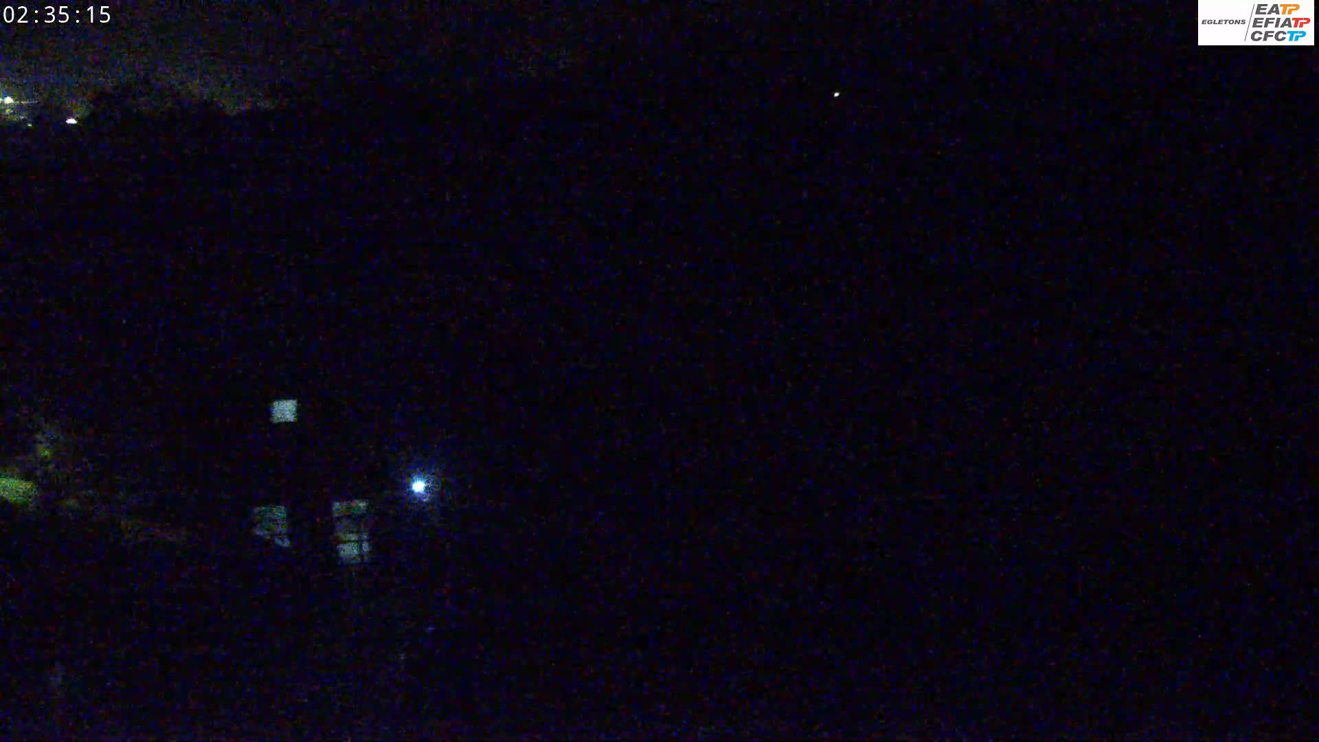 A nighttime long shot shows a dark landscape with a few small lights visible in the distance, and a brighter light closer to the camera's position.