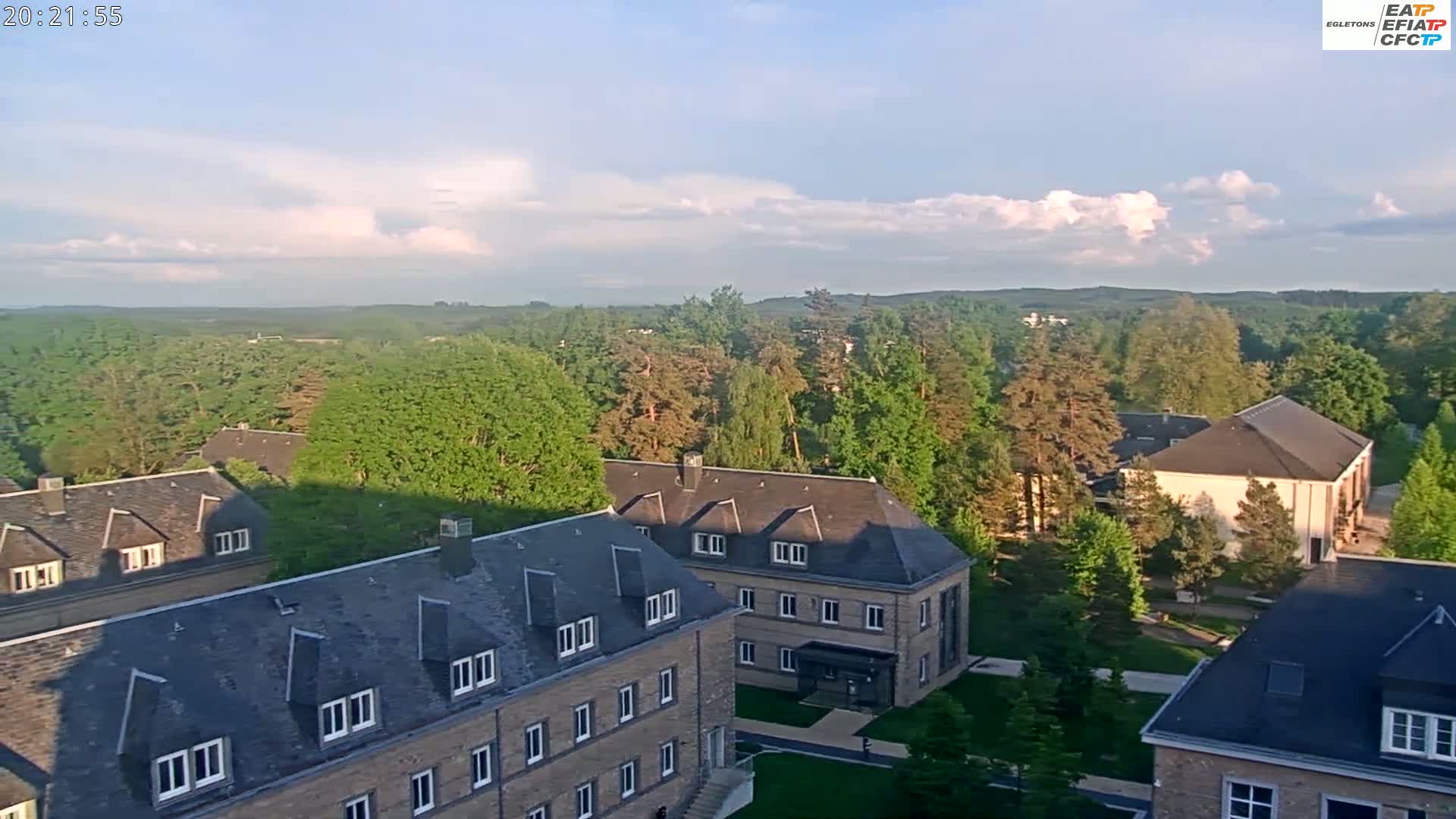 An elevated view of several stone buildings surrounded by lush green trees under a partly cloudy sky.