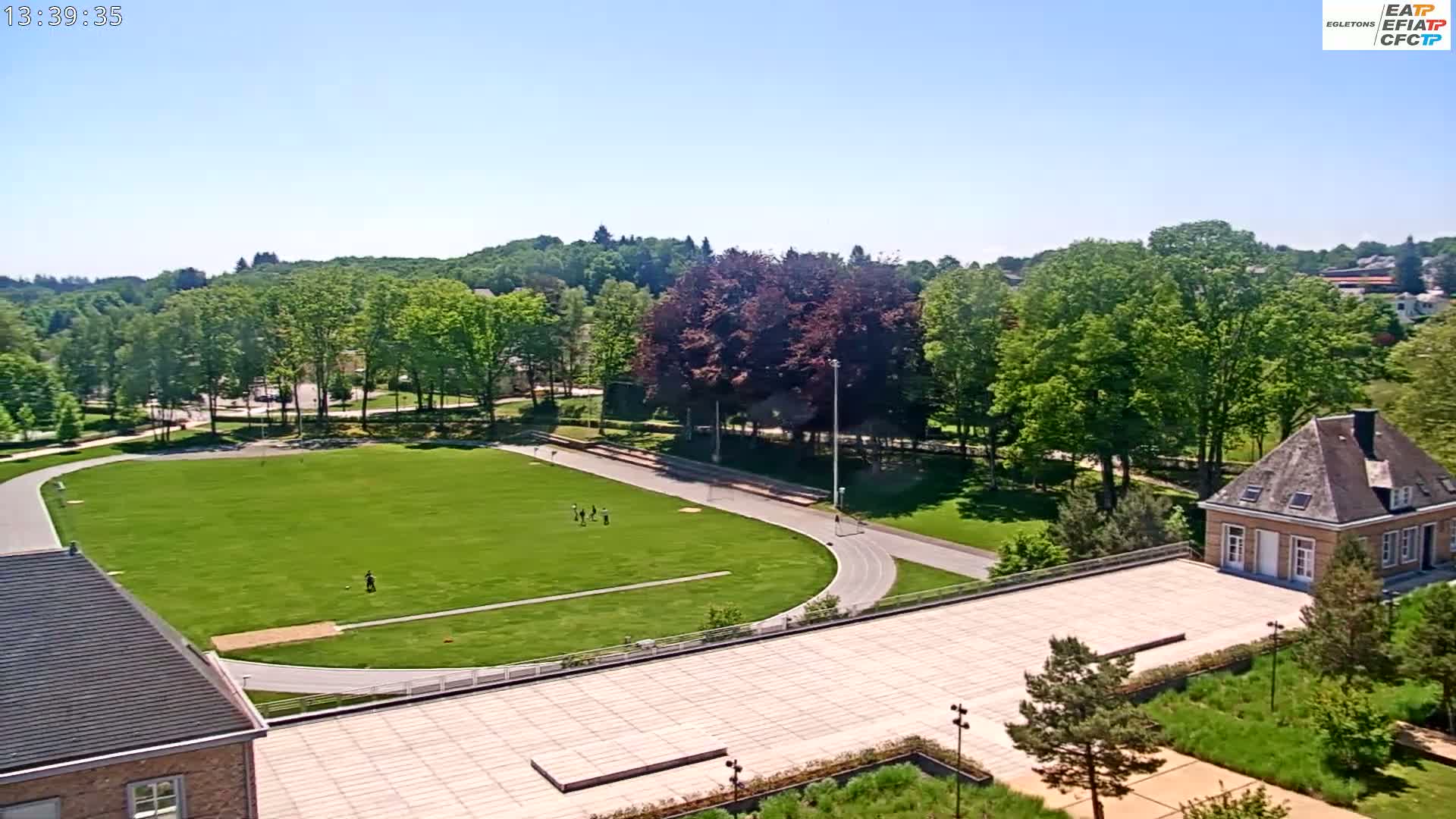 A grassy field with a running track surrounds a building on a sunny day.