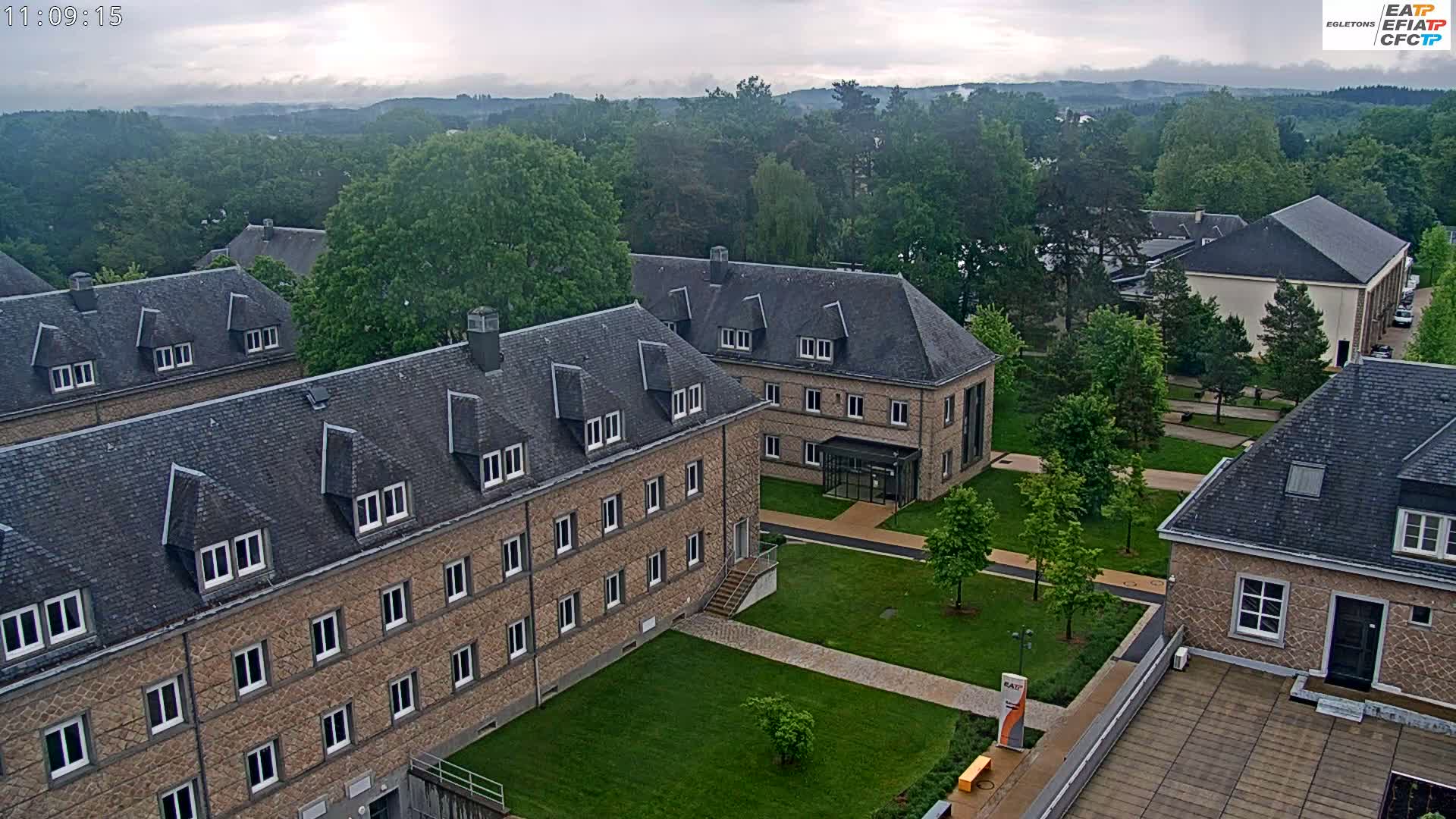 An aerial view of a campus with several stone buildings, green lawns, and trees under an overcast sky.