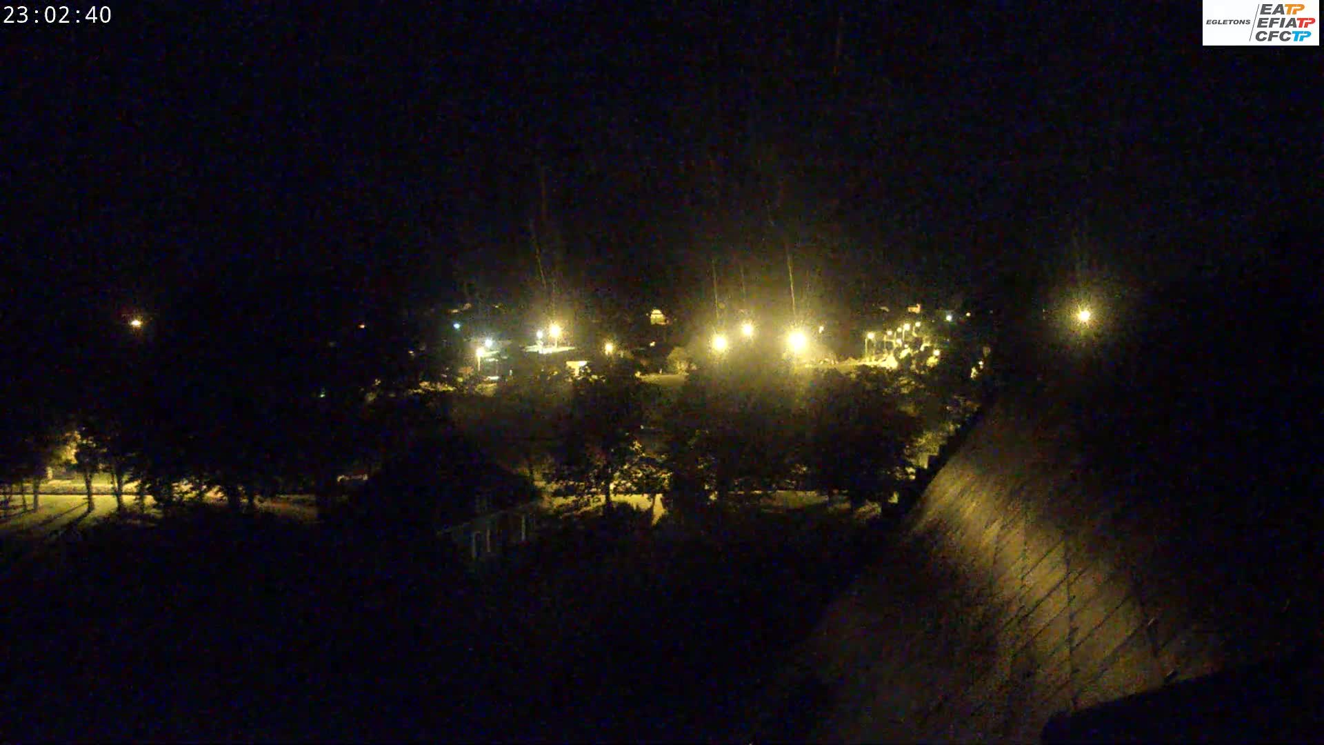 A nighttime aerial view of a dark, tree-lined area with sparsely lit buildings and streets.