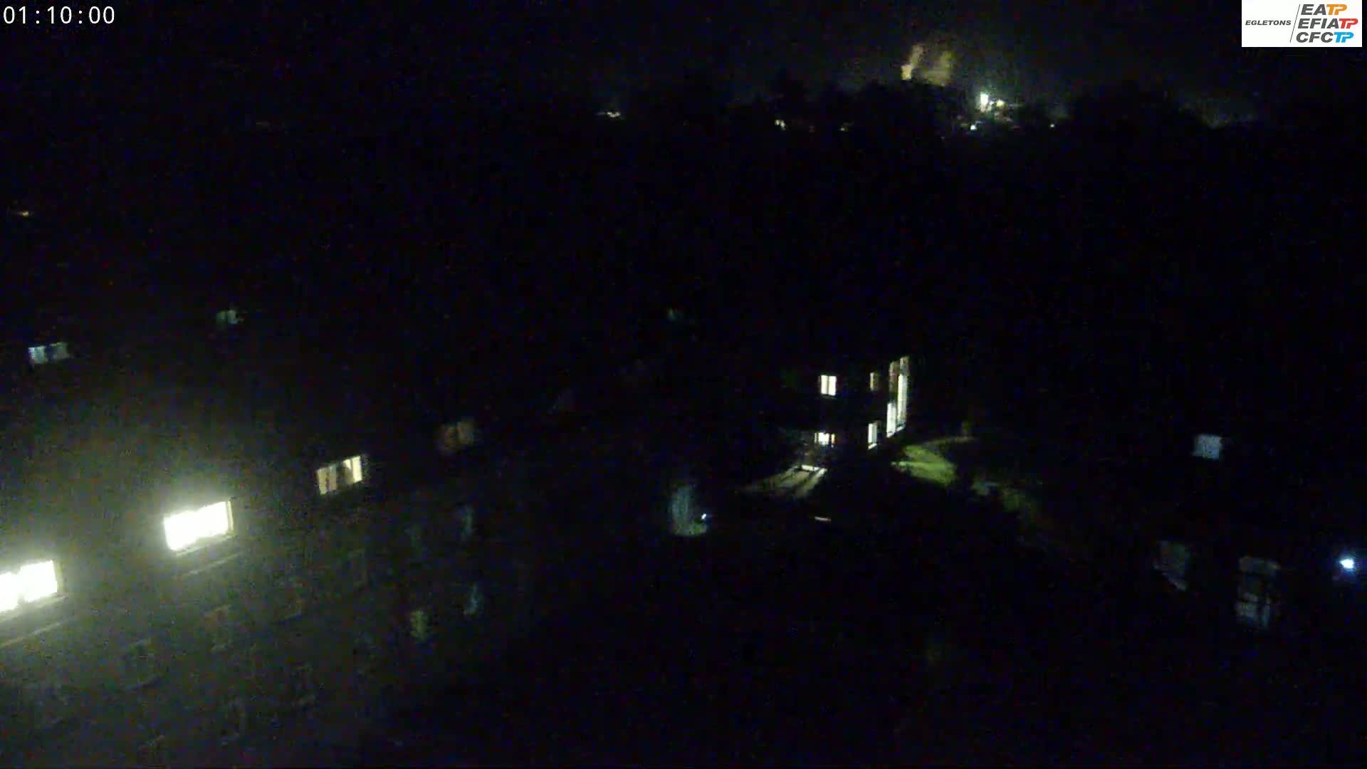 A nighttime aerial view shows a residential area with dimly lit windows and a dark, overcast sky.
