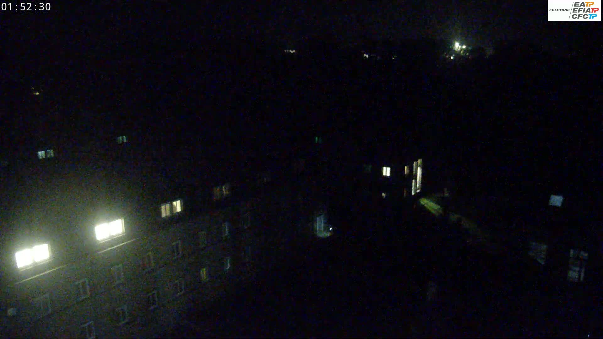 A nighttime, aerial view shows a dark cityscape with several buildings, some with illuminated windows.