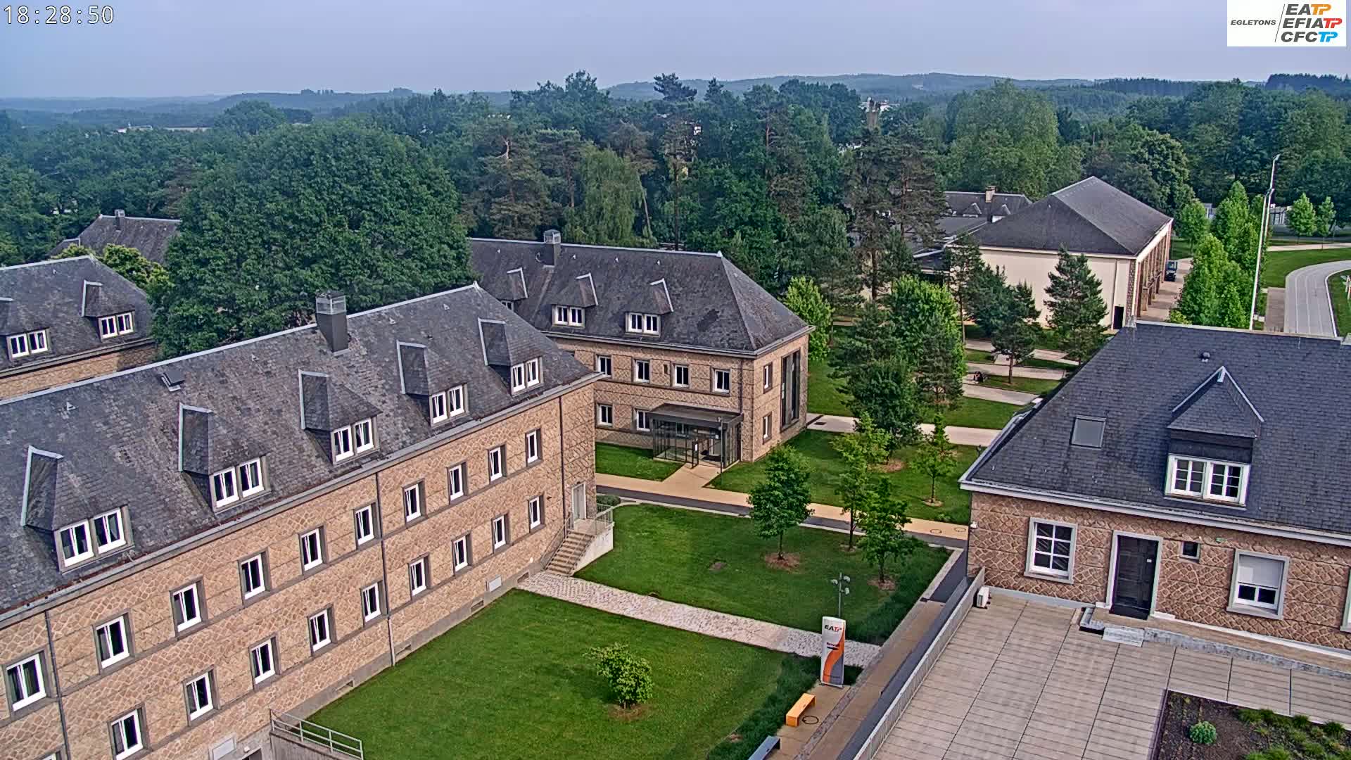 An aerial view of a campus with several stone buildings on a partly cloudy day, surrounded by green lawns and trees.