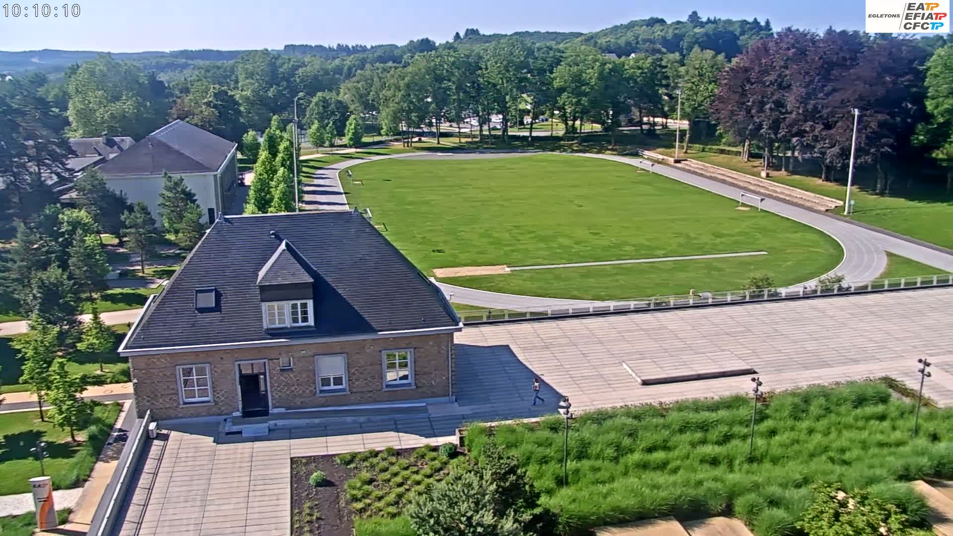 A sunny day reveals a grassy athletic field with a running track, surrounding buildings, and landscaped grounds.