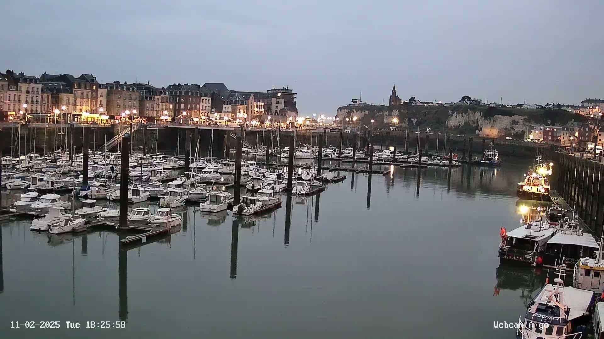 A harbor filled with numerous docked boats is illuminated at dusk under a twilight sky.