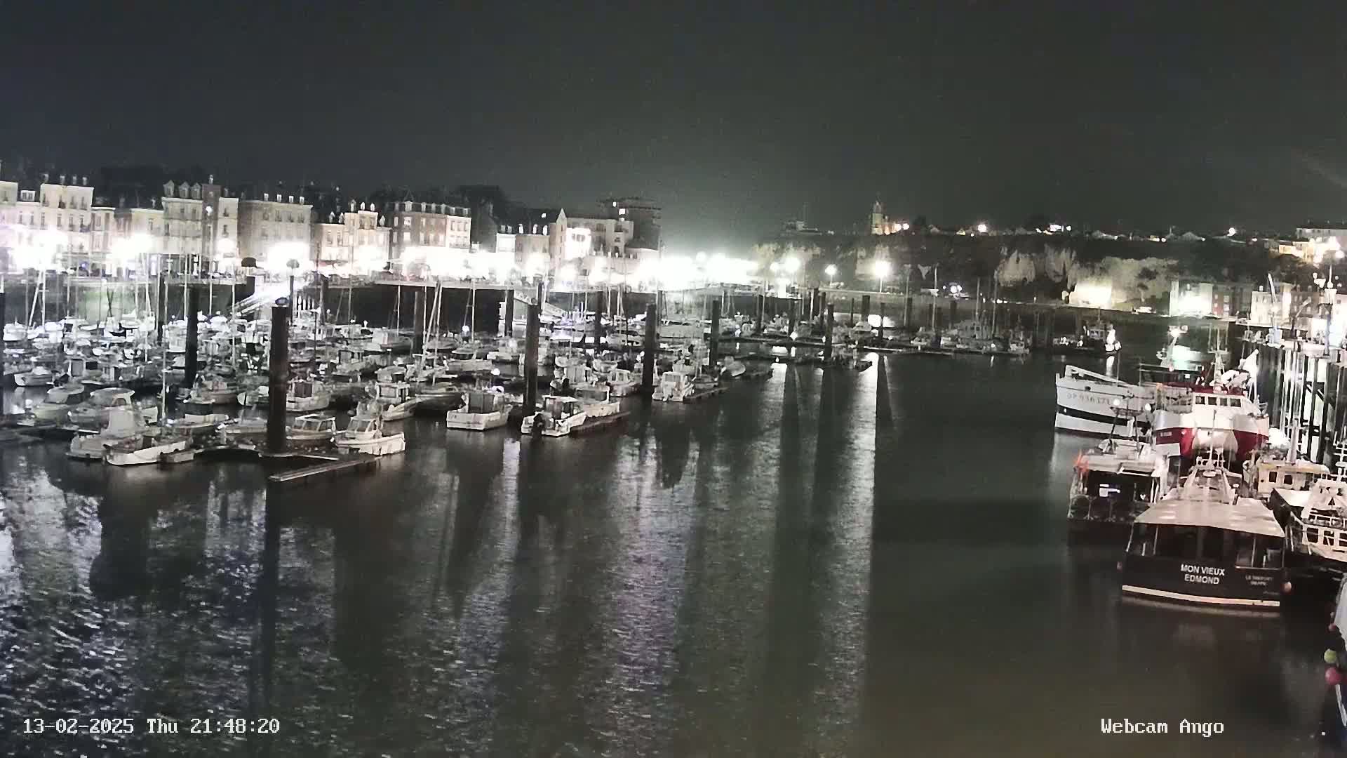 A nighttime view of a harbor filled with docked boats and illuminated buildings along the shoreline.