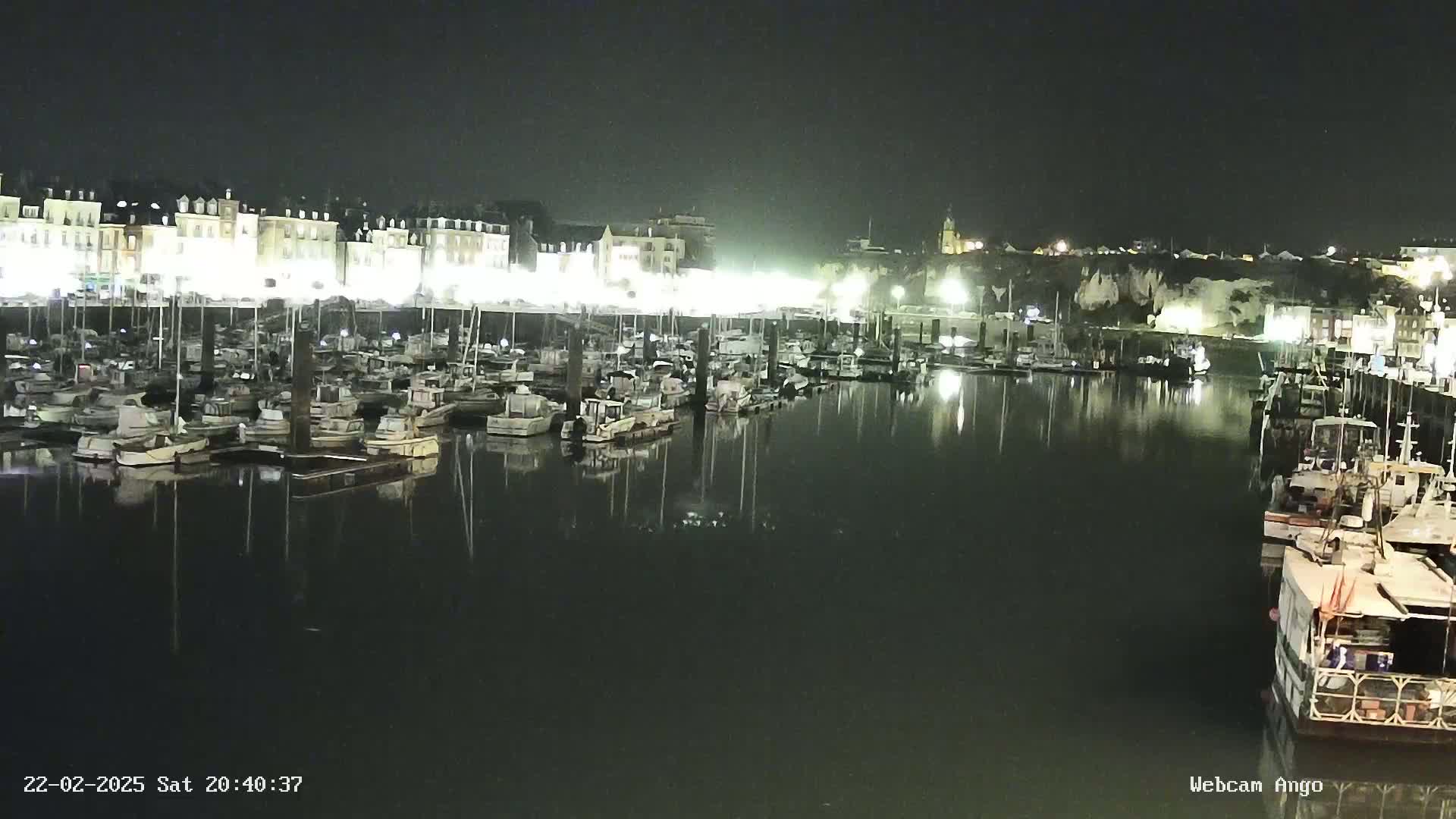 A nighttime view of a harbor filled with numerous boats docked alongside a brightly lit waterfront.