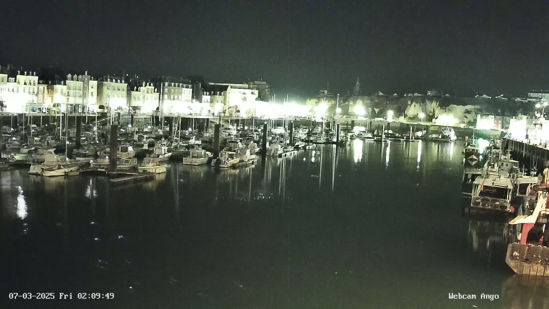 A nighttime view of a harbor filled with docked boats and illuminated buildings along the waterfront.