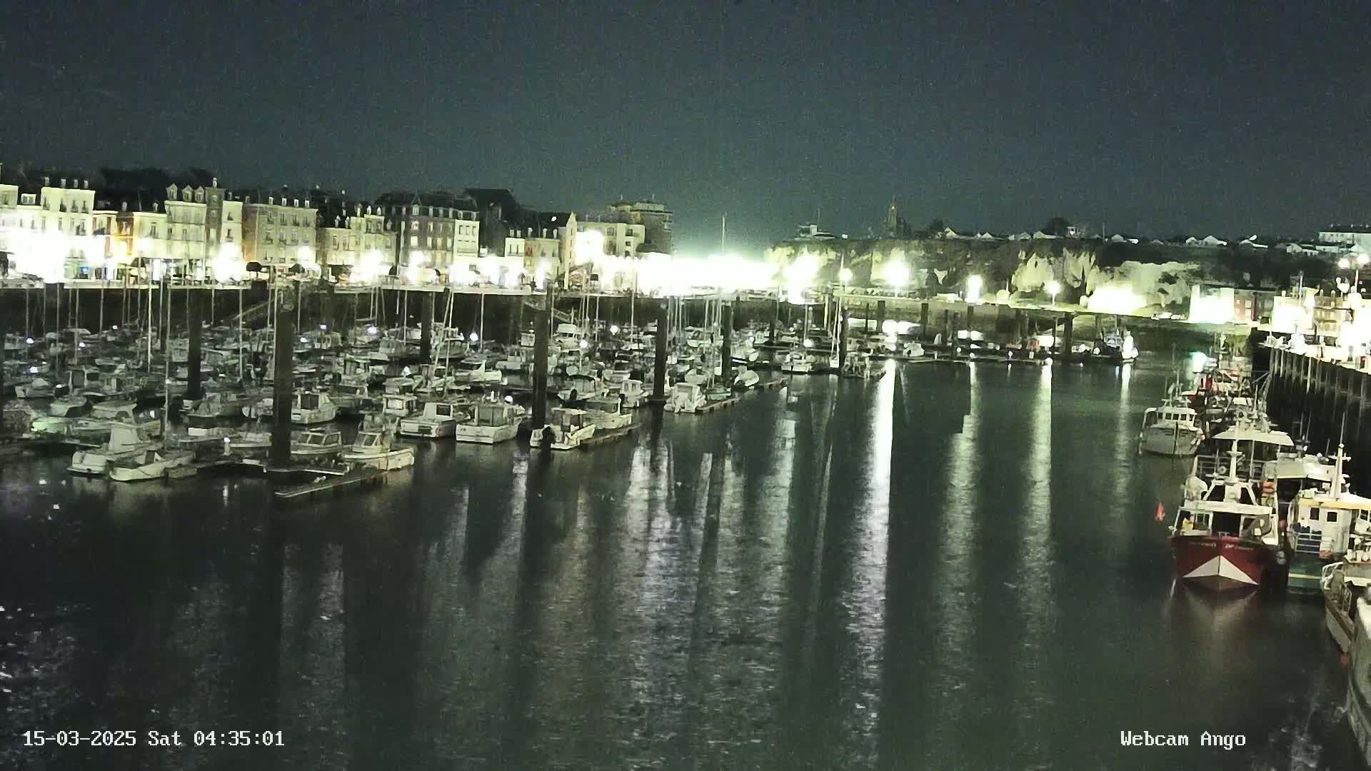A nighttime harbor filled with numerous boats, illuminated by lights along a waterfront building.