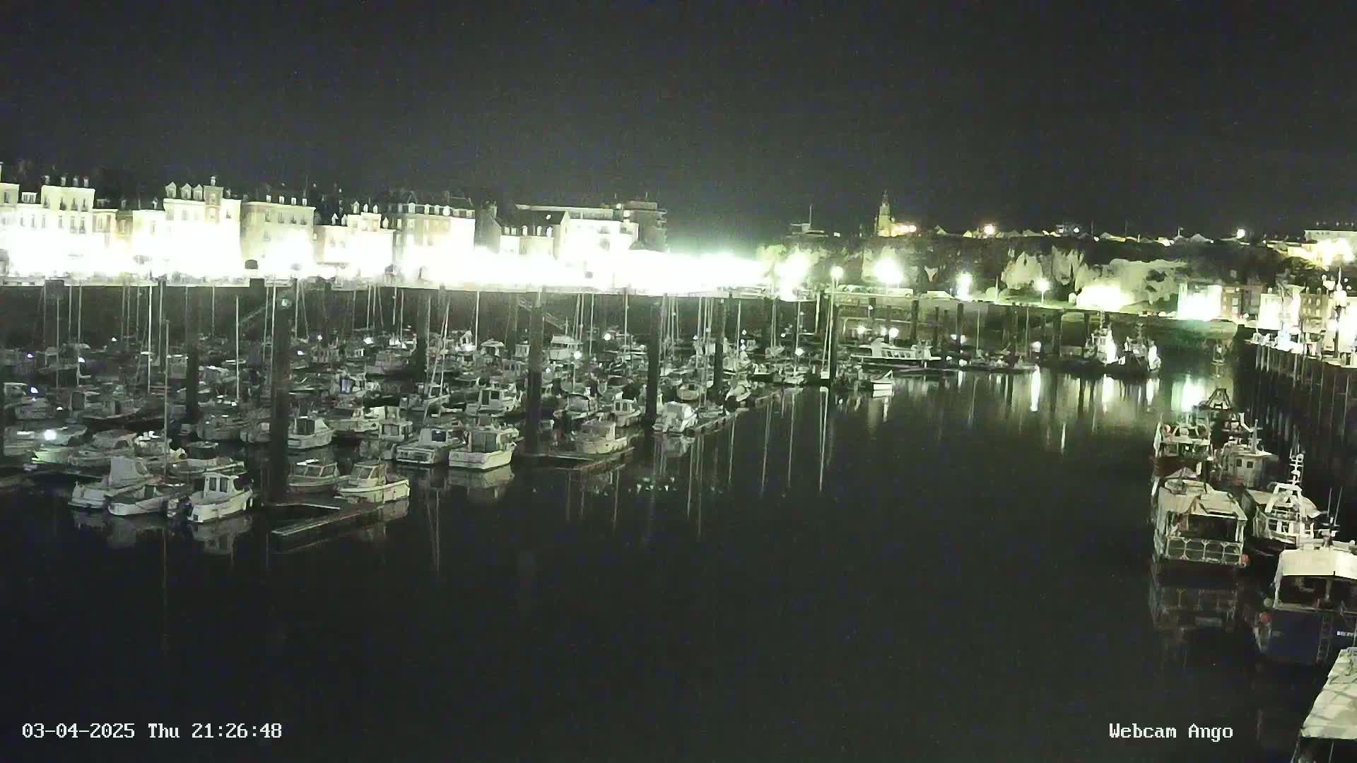 A nighttime harbor filled with many docked boats, illuminated by lights along a waterfront building.