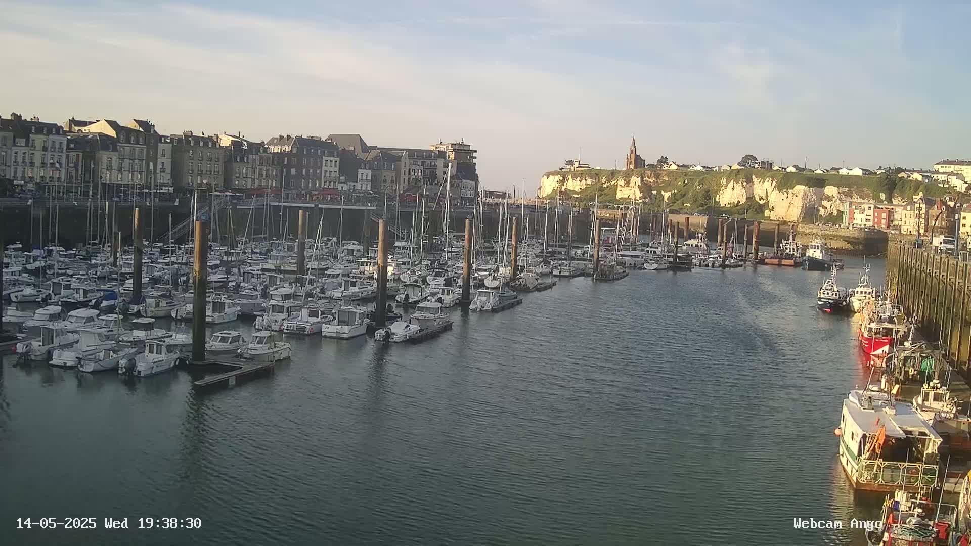 A harbor filled with many docked boats is situated next to a town under a partly cloudy sky.