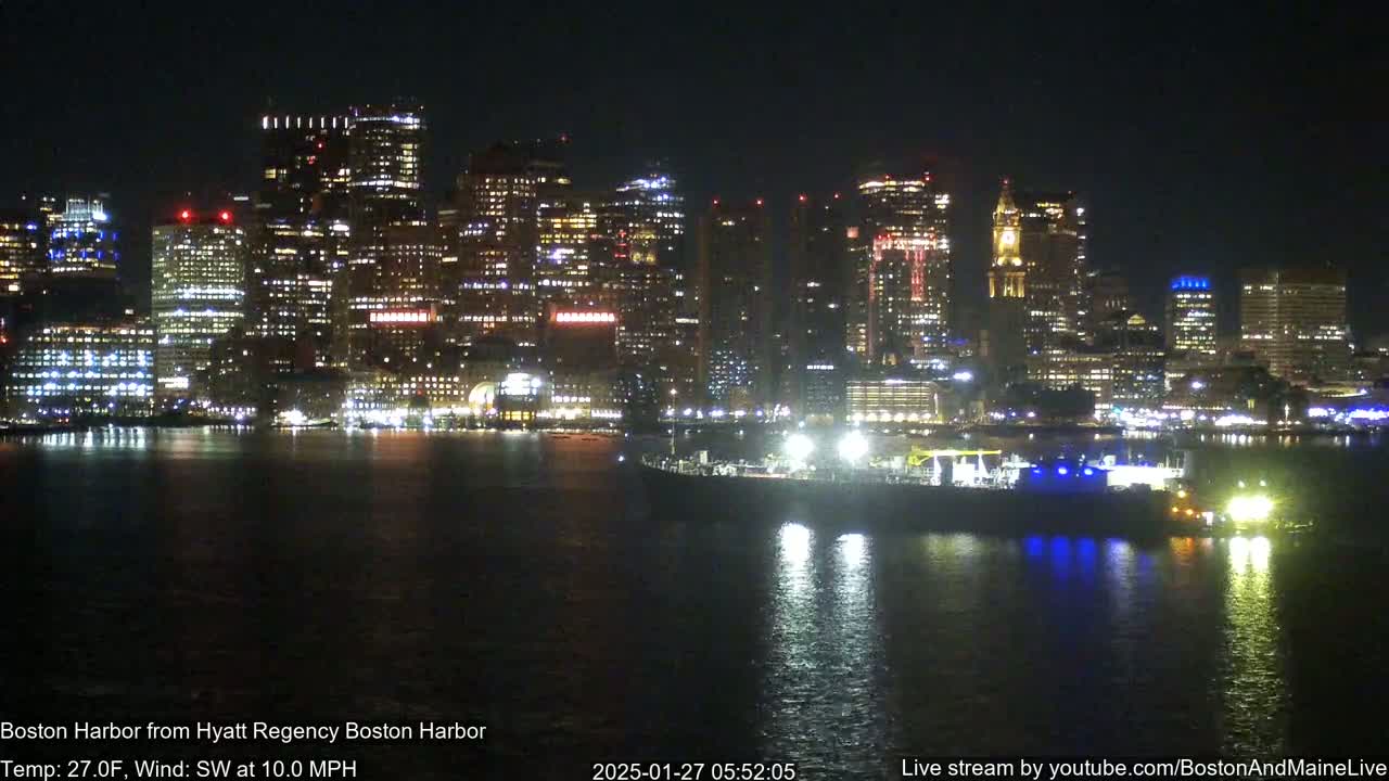 A brightly lit cityscape is seen across a dark body of water at night, with a southwest wind blowing at 10 mph and a temperature of 27 degrees Fahrenheit.