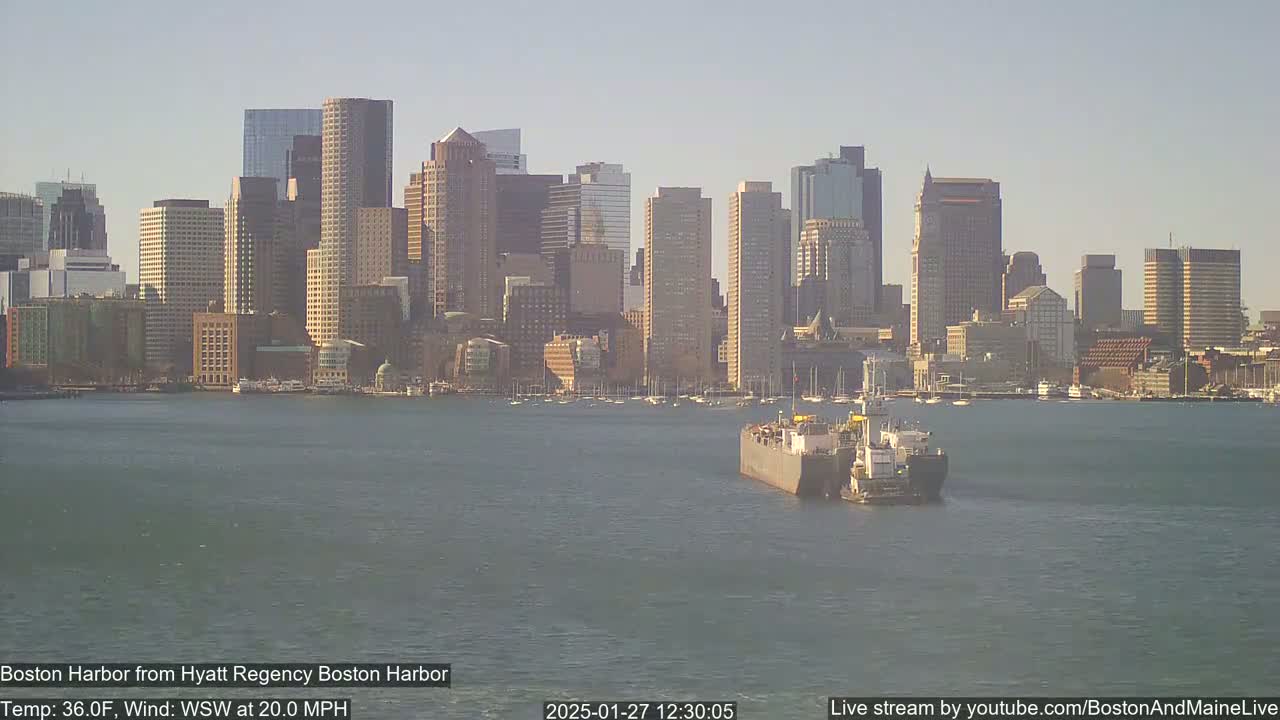 A barge travels across a harbor toward a city skyline on a partly sunny day with a 20 mph wind from the west-southwest.