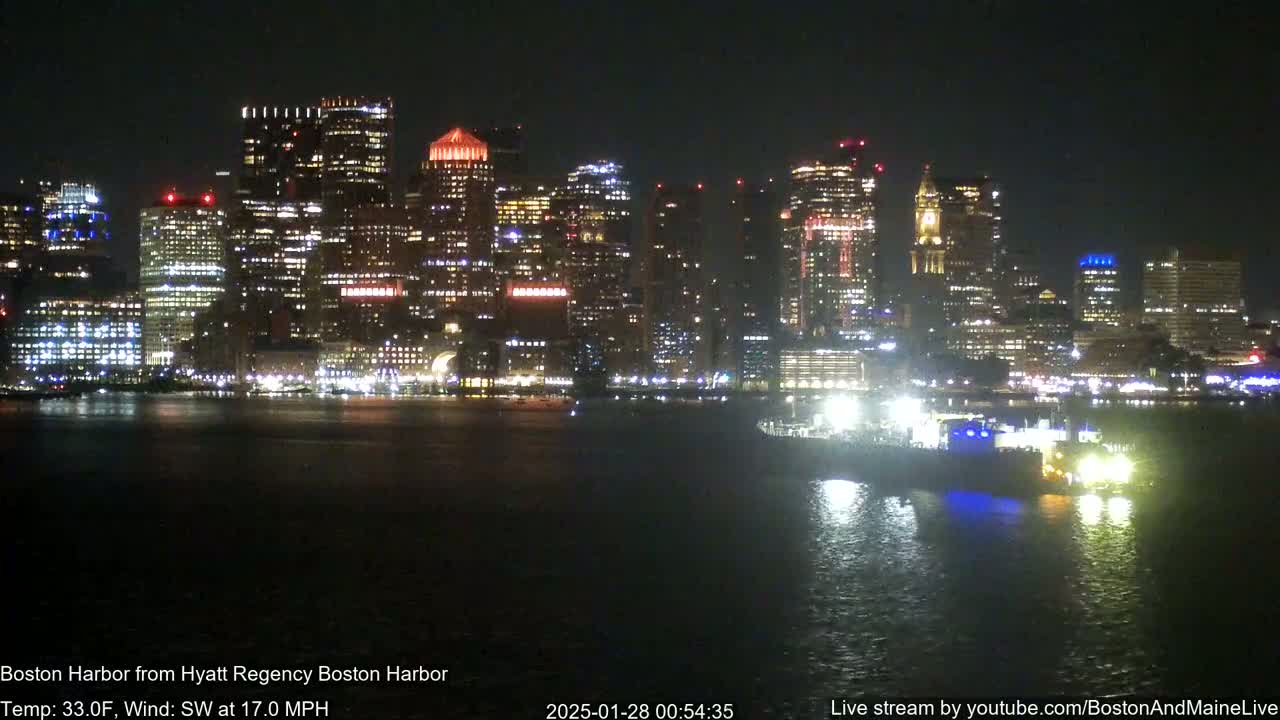 A brightly lit city skyline is reflected on dark water at night, with a southwest wind blowing at 17 mph.