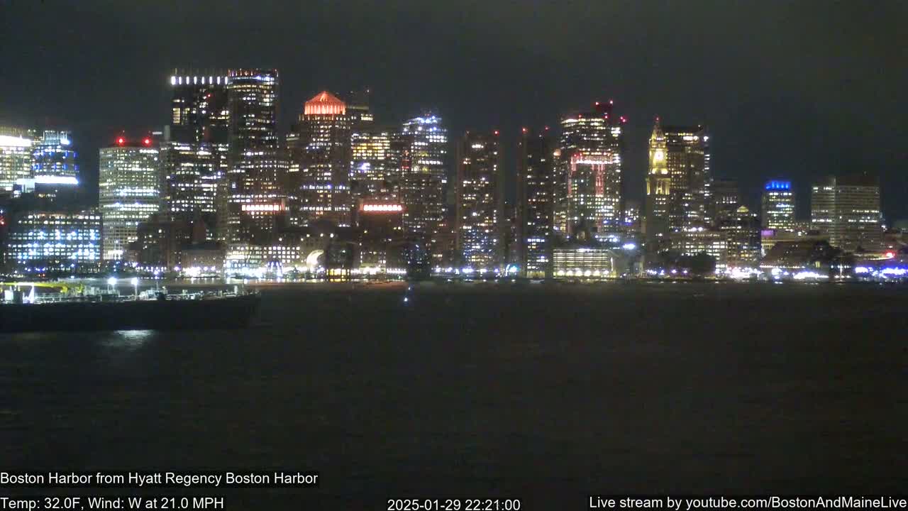 A nighttime view of a city skyline across a dark body of water, with a 32°F temperature and a 21 mph west wind.