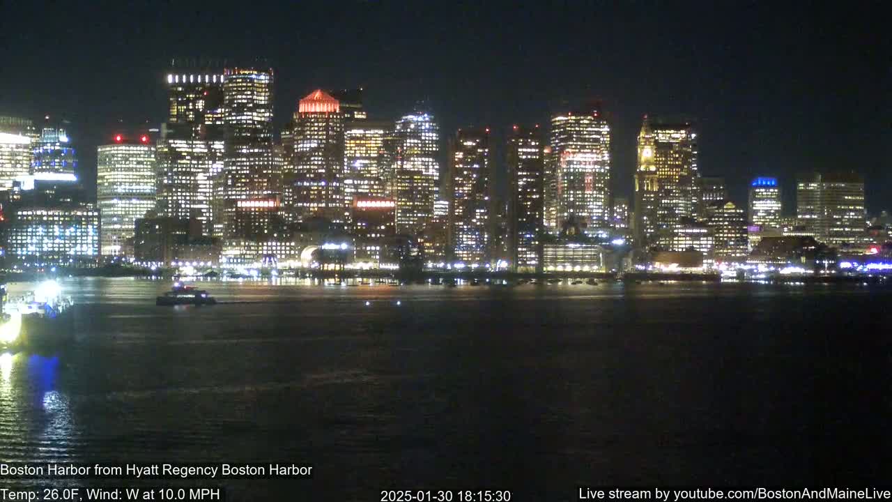 A brightly lit cityscape is seen across a dark body of water at night, with a 10 mph west wind and a temperature of 26°F.