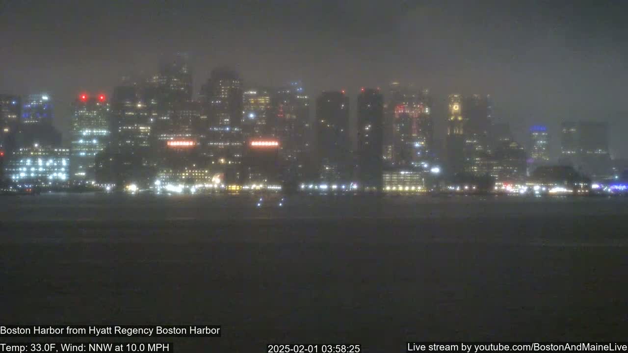 A nighttime cityscape is seen across a body of water during snowy conditions.