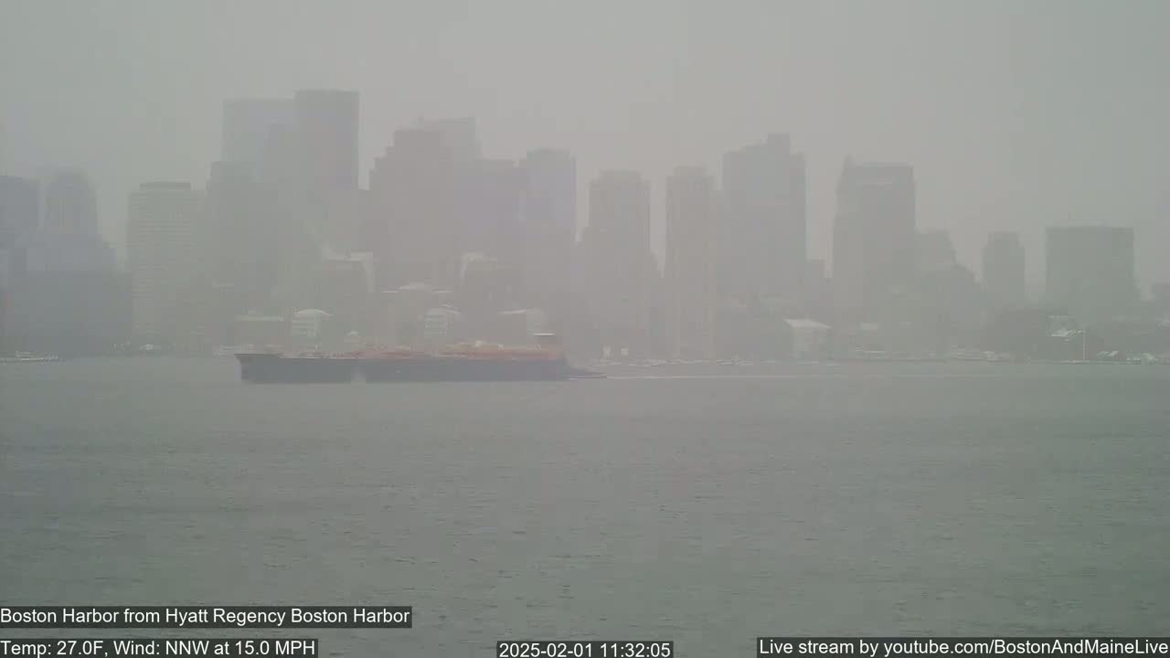 A hazy, gray cityscape is seen across a body of water, with a large ship in the foreground and a 15 mph north-northwest wind.