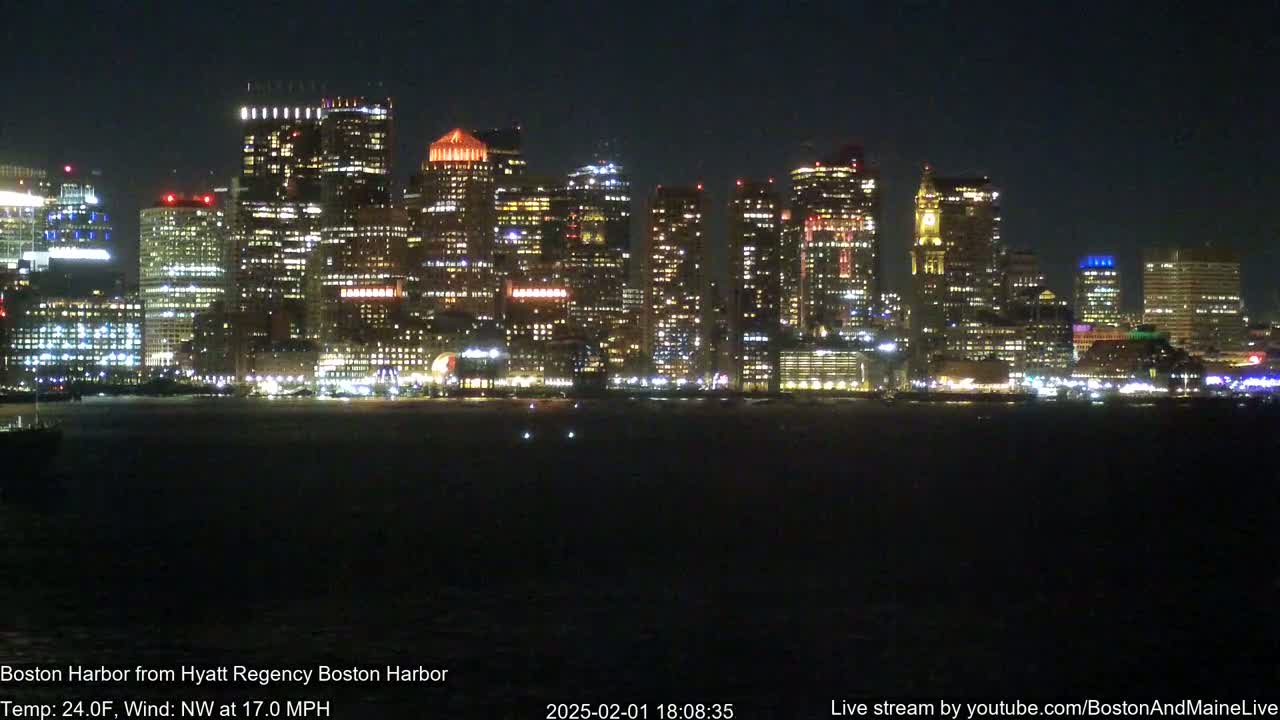 A brightly lit cityscape is seen across a dark body of water at night, with a northwest wind at 17 miles per hour and a temperature of 24 degrees Fahrenheit.