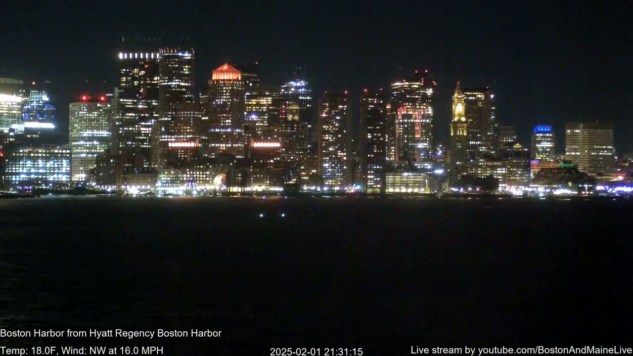 A nighttime view of a brightly lit city skyline across a dark body of water, with a northwest wind at 16 mph and a temperature of 18°F.