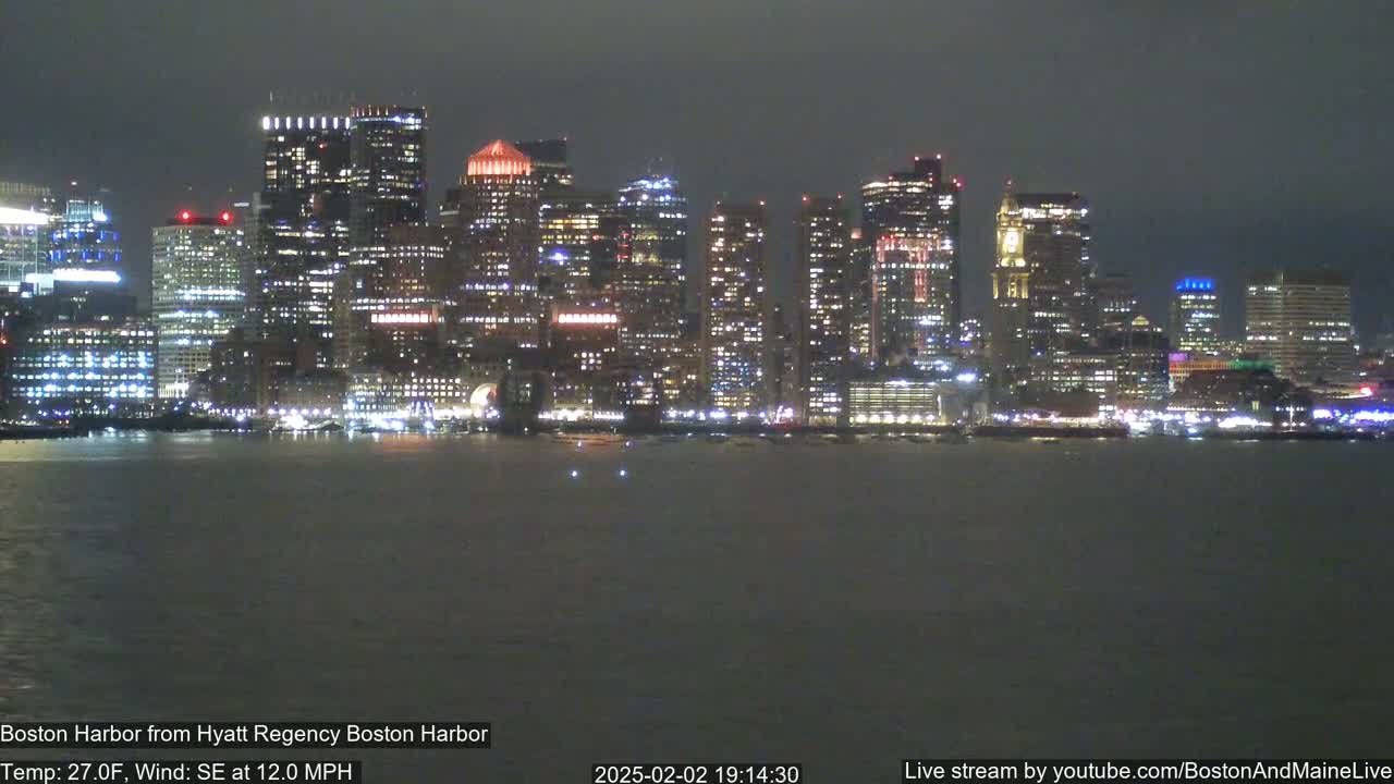 A nighttime view of a city skyline across a dark body of water, under a cloudy sky with a southeast wind at 12 mph and a temperature of 27°F.