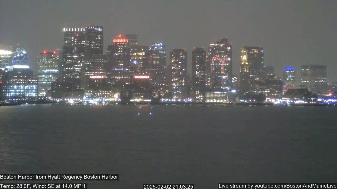 A nighttime view of a city skyline across a dark body of water, under a slightly hazy sky with a southeast wind of 14 mph and a temperature of 28°F.