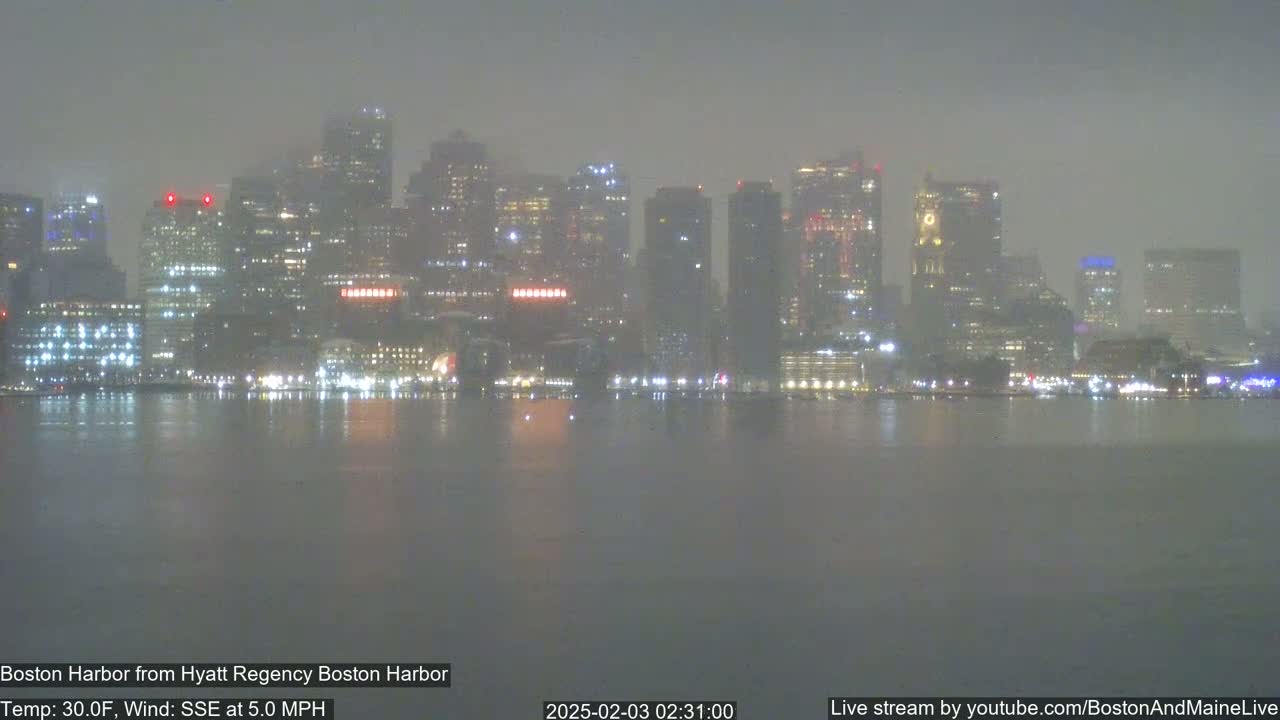 A hazy, nighttime view of a city skyline across a body of water, with a temperature of 30°F and a 5 mph wind from the south-southeast.