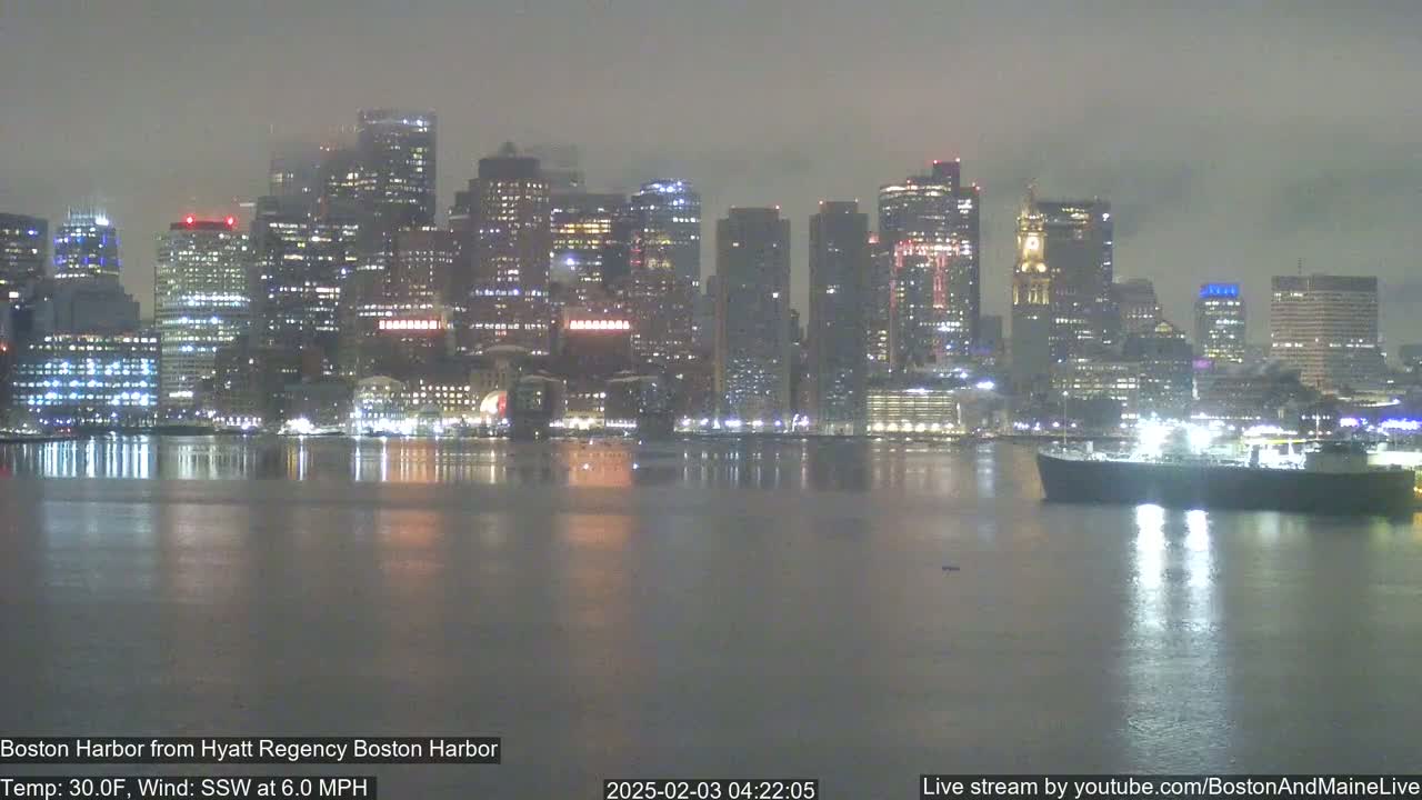 A nighttime view of a city skyline across a calm harbor under a hazy sky.