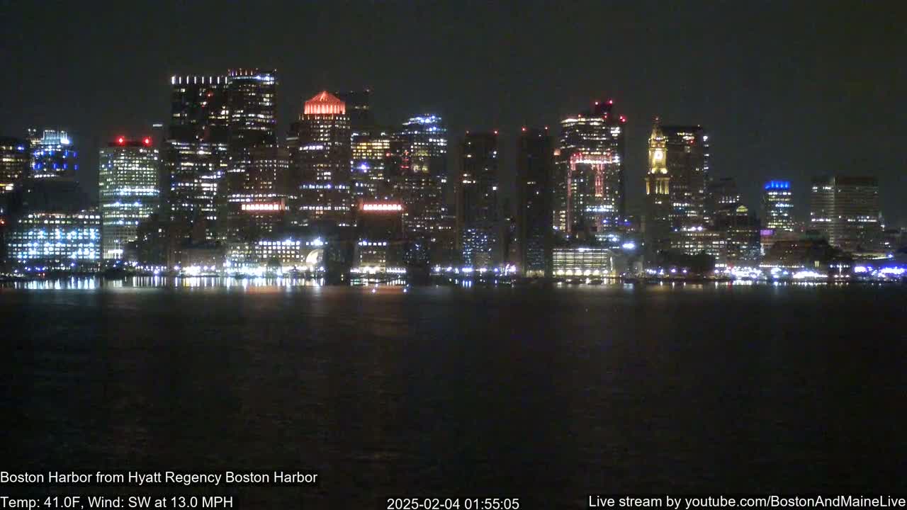 A brightly lit city skyline is seen across a dark body of water at night, with a southwest wind blowing at 13 mph and a temperature of 41°F.