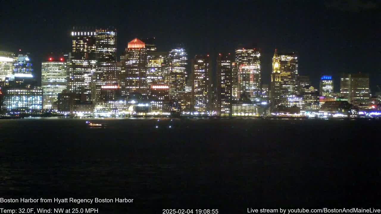 A brightly lit city skyline is visible across a dark body of water at night, under a dark sky with a 25 mph northwest wind and a temperature of 32 degrees Fahrenheit.