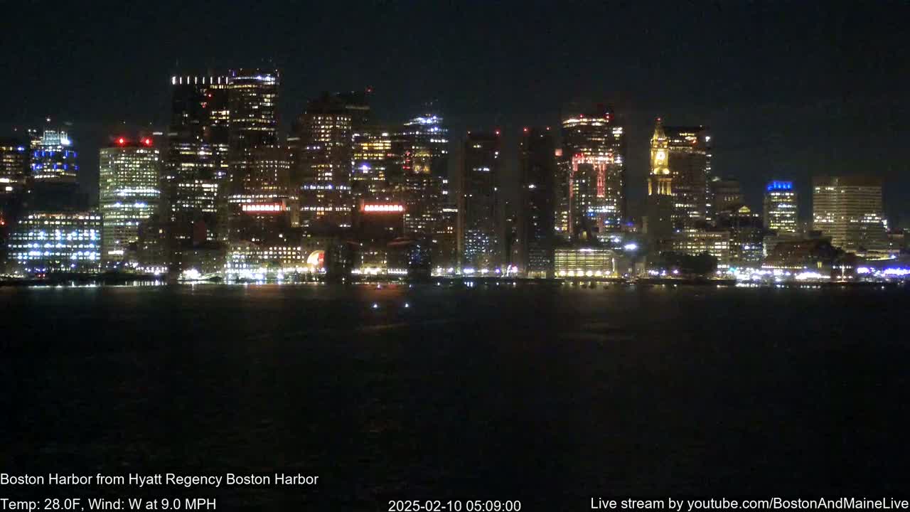 A brightly lit cityscape is seen across a dark body of water at night, with a westerly wind blowing at 9.0 mph and a temperature of 28°F.