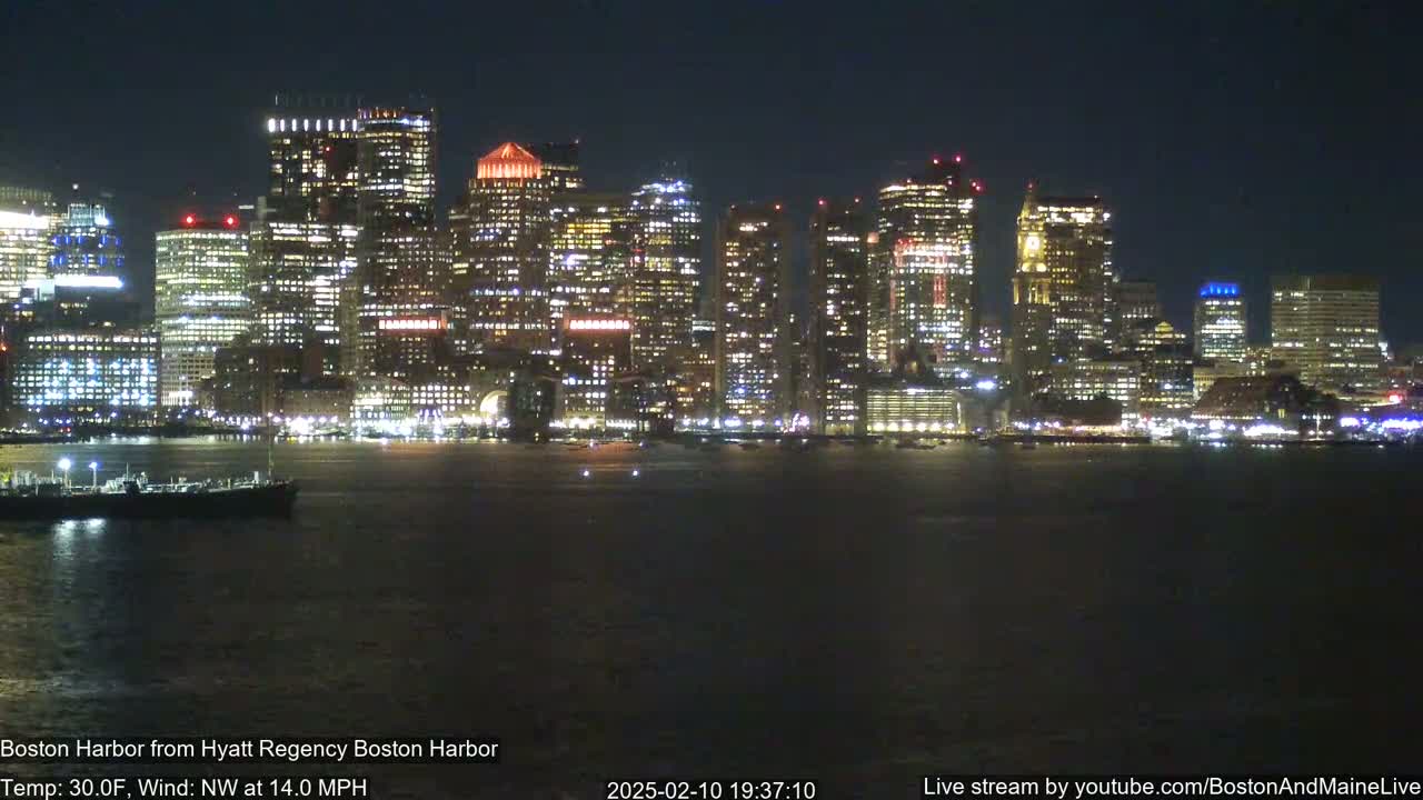 A nighttime view of a city skyline across a dark body of water, under a clear sky with a northwest wind at 14 mph and a temperature of 30°F.