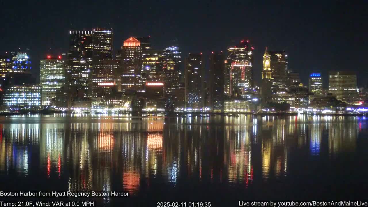 A nighttime cityscape with brightly lit buildings reflected in a calm body of water under a clear, dark sky.