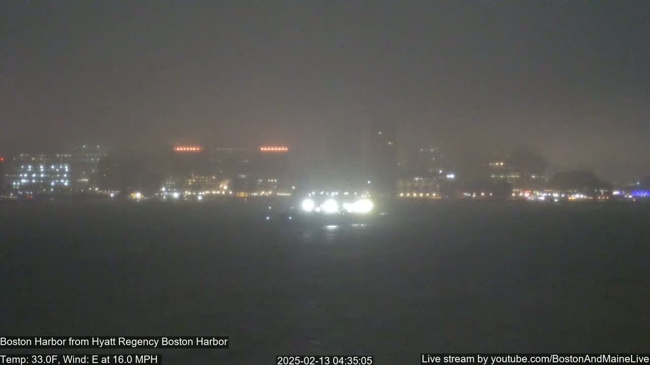 A hazy, nighttime view of a city skyline across a dark body of water, with a 16 mph east wind and a temperature of 33 degrees Fahrenheit.