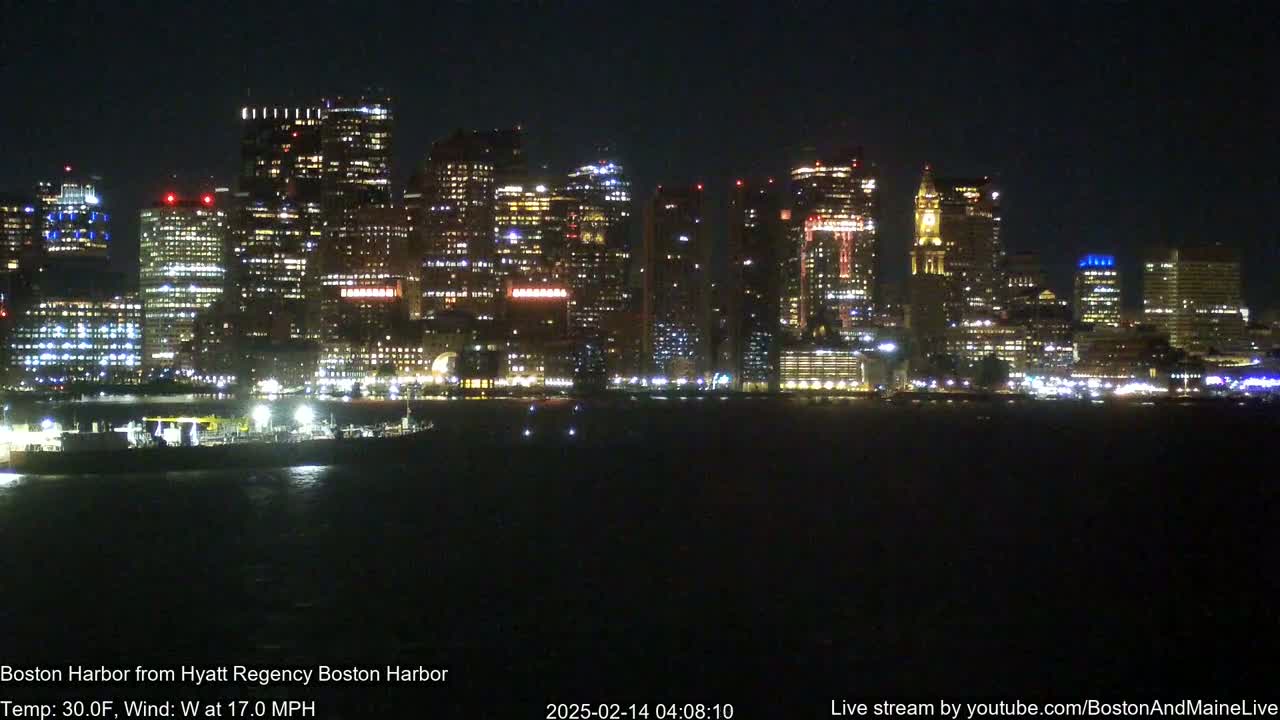 A brightly lit cityscape is seen across a dark body of water at night, with a 30°F temperature and 17 mph west wind.