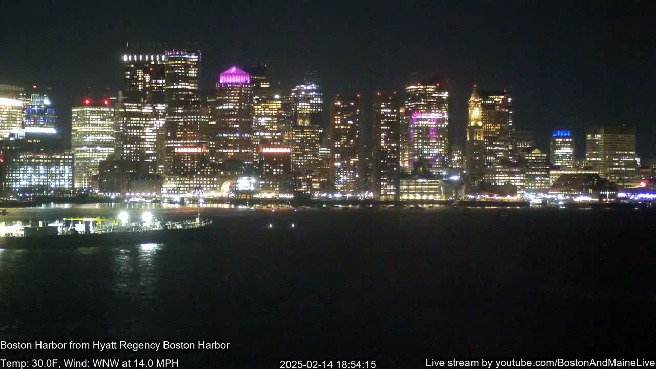 A nighttime view of a brightly lit city skyline across a dark body of water, under a clear sky.