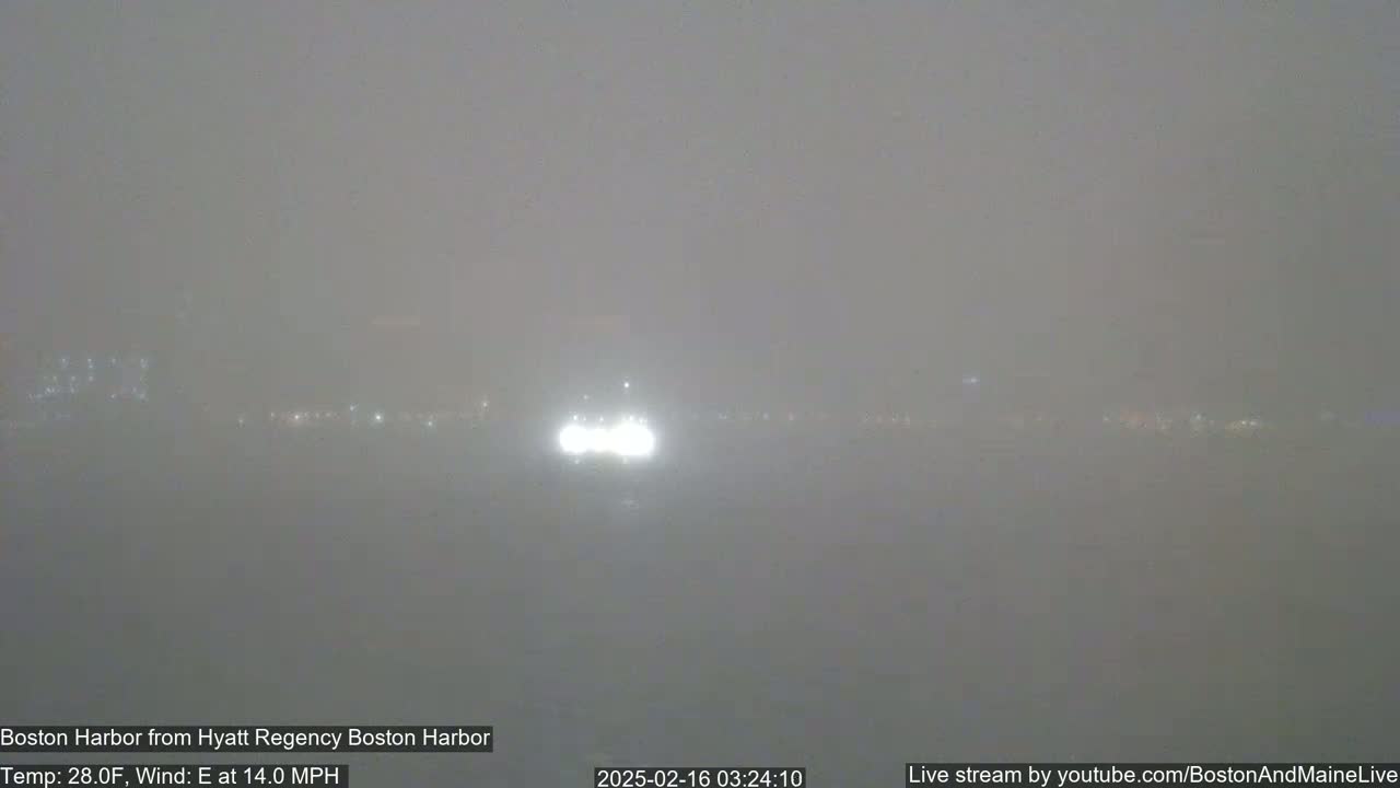 A hazy, foggy harbor scene at night is visible, with faint lights in the distance and a strong easterly wind.